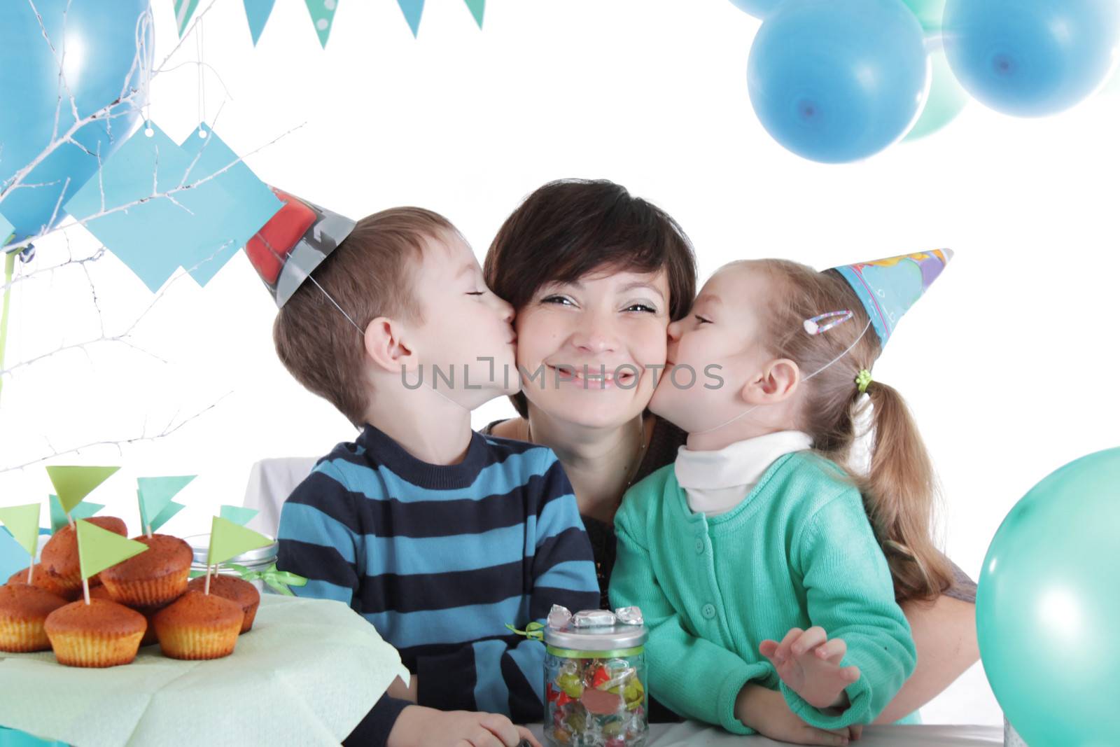 Two children kissing their mother at party table isolated on white
