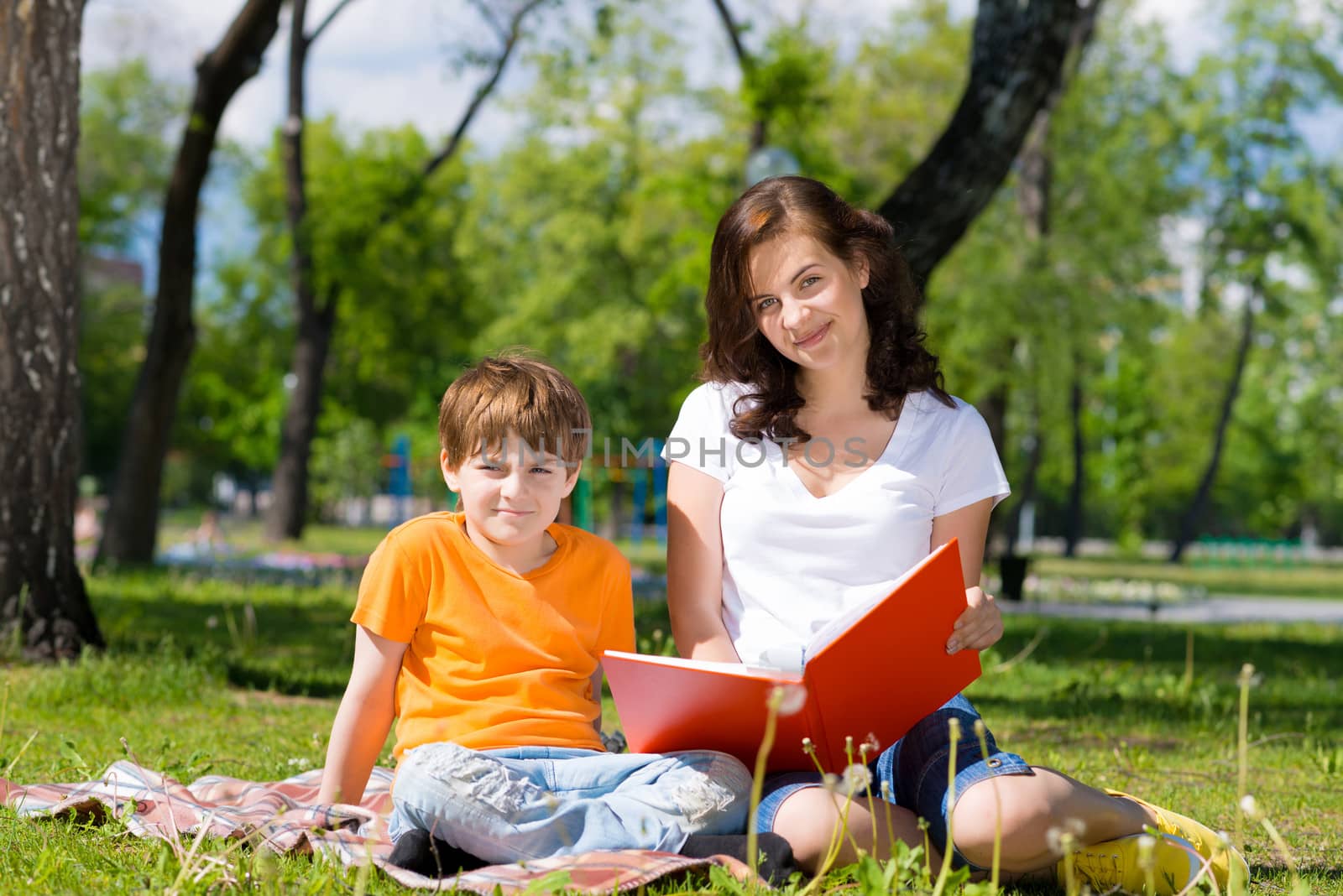 boy and a woman in a summer park reading a book together