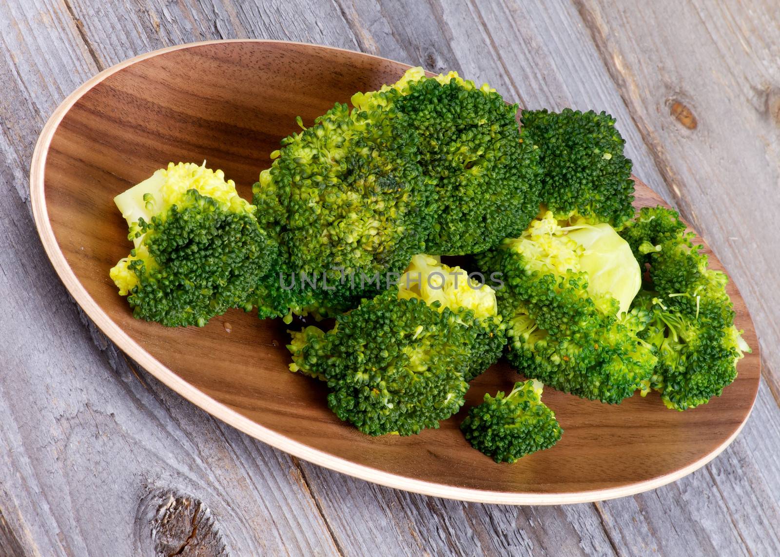 Tasty Ready-to-Eat Boiled Broccoli on Wooden Plate isolated on Rustic Wood background