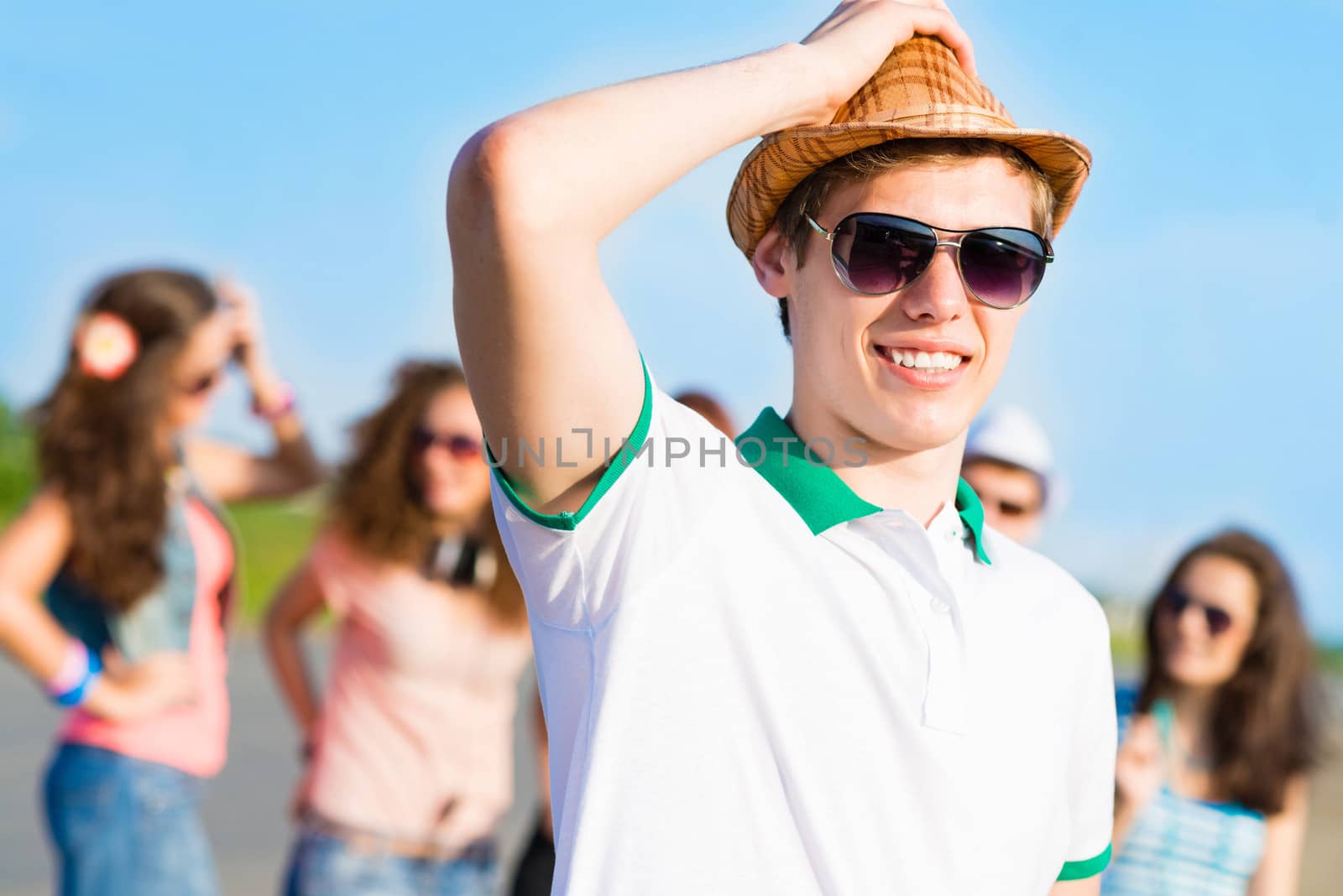 young man in sunglasses, a hat holds a hand on a background of blue sky and friends