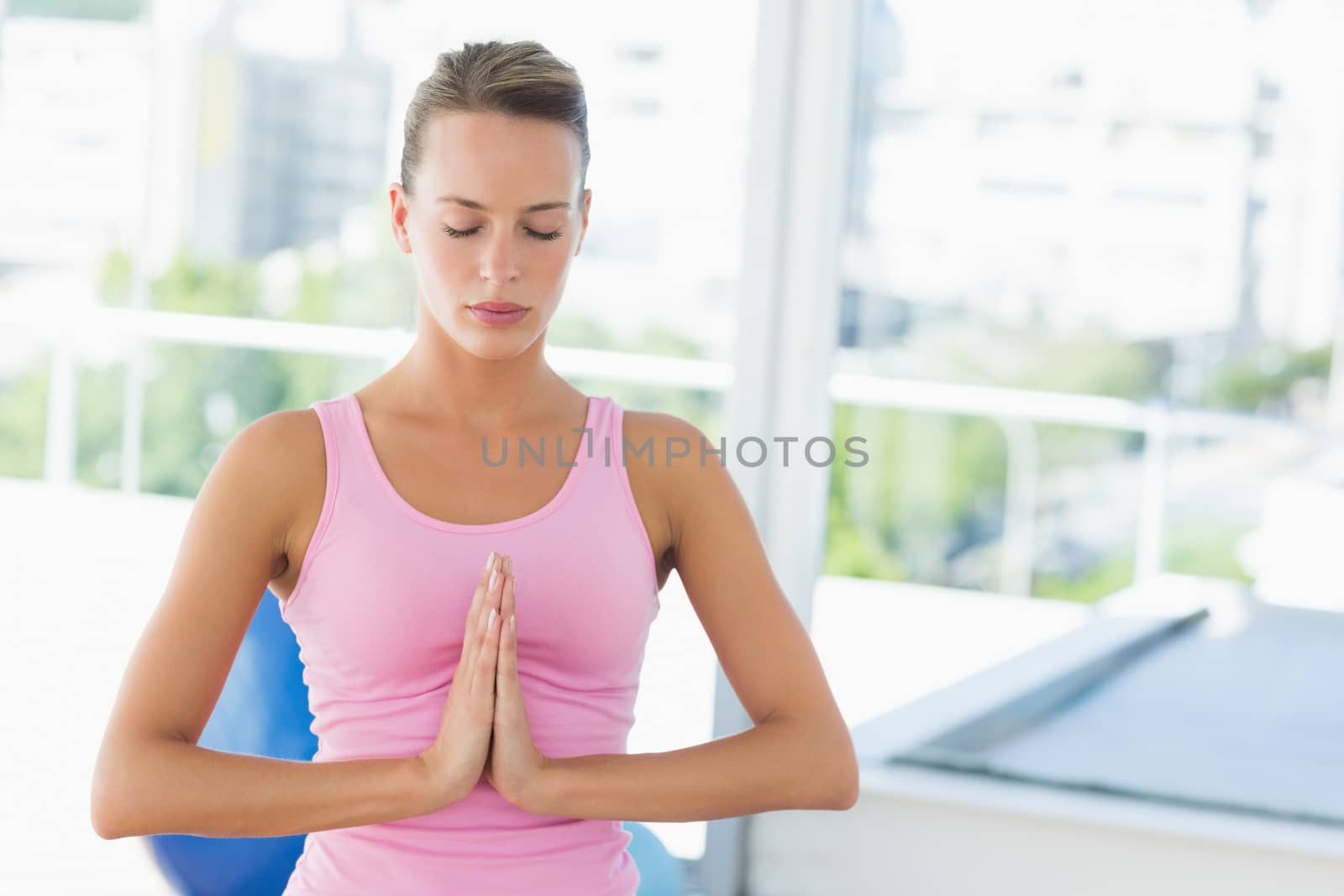 Serious young woman with joined hands and eyes closed at a bright fitness studio