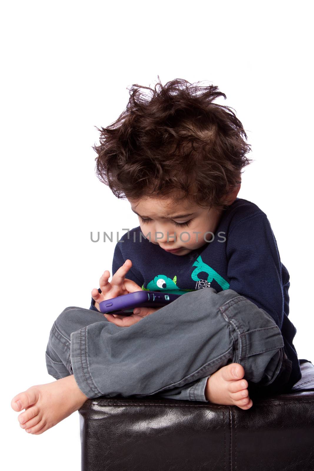 Cute toddler boy sitting playing games on mobile device and crazy hair, isolated.