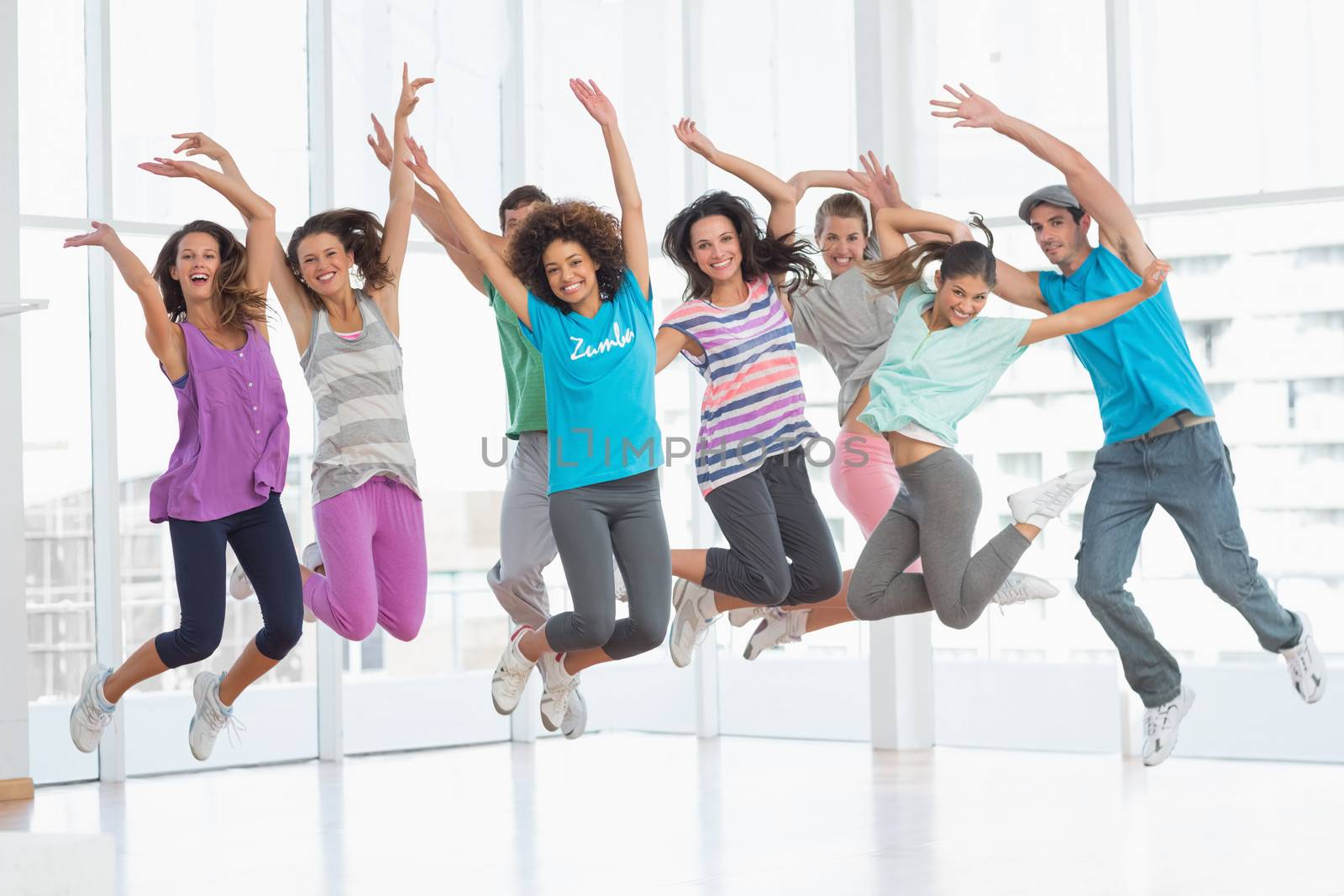 Full length portrait of fitness class and instructor jumping in fitness studio