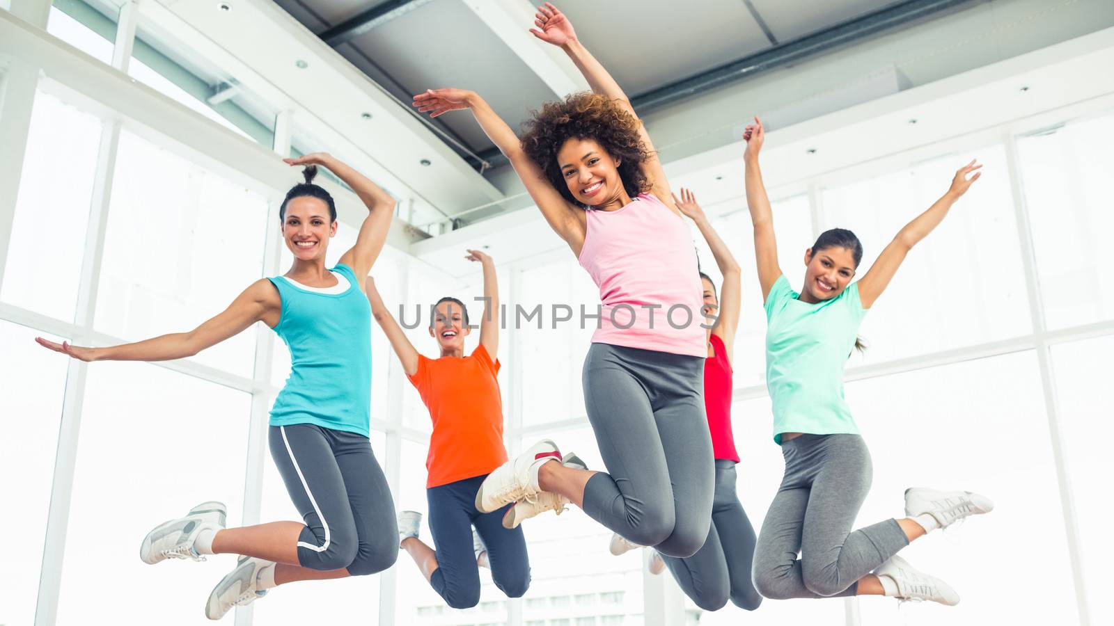 Full length portrait of fitness class and instructor jumping in fitness studio