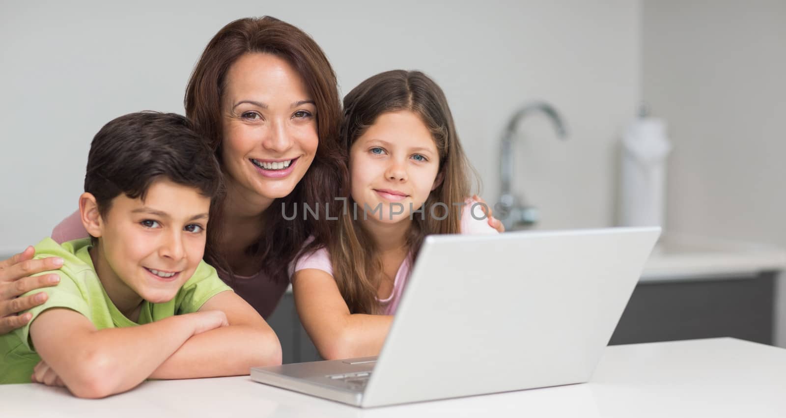 Portrait of a smiling mother with young kids using laptop in the kitchen at home