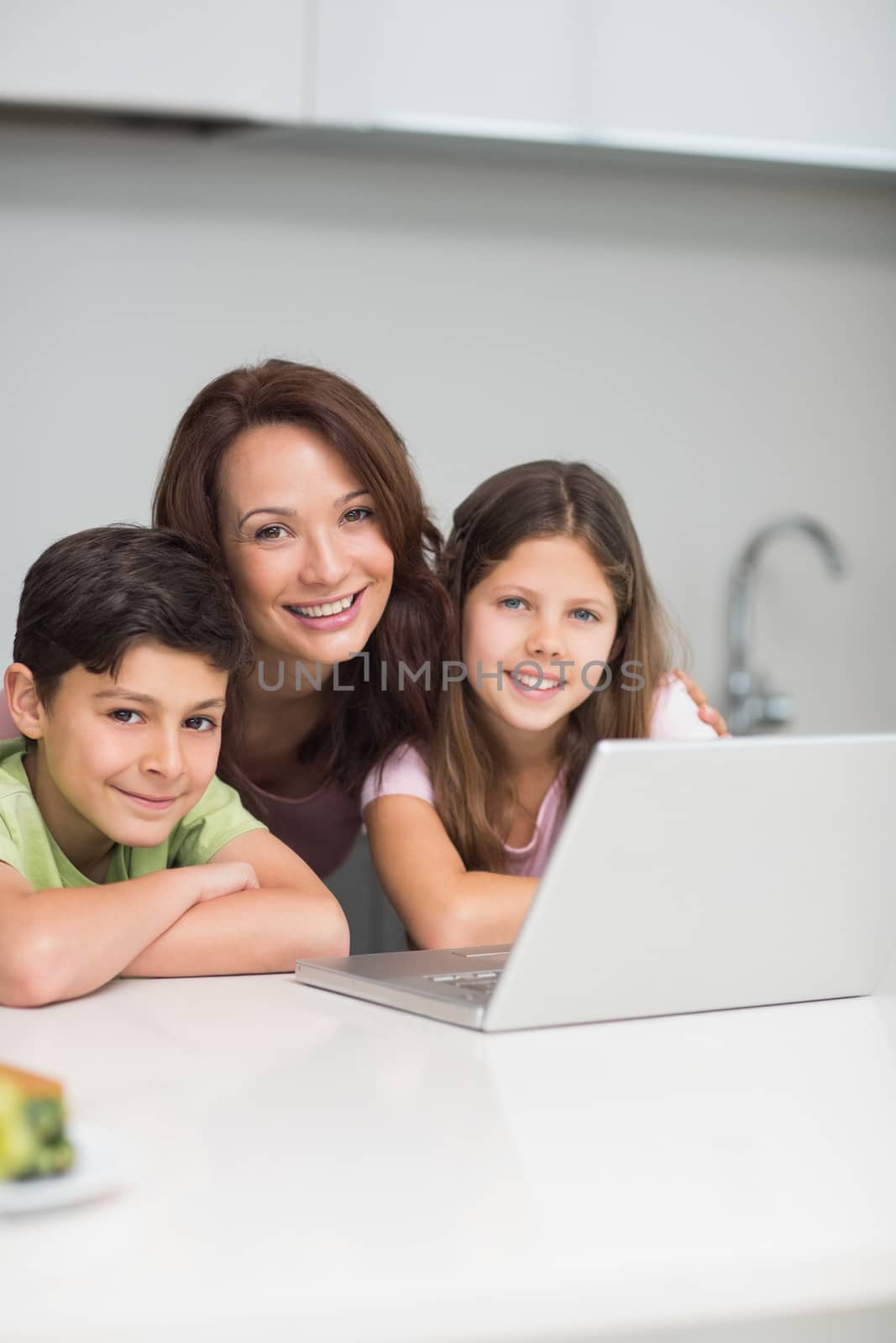 Smiling mother with kids using laptop in kitchen by Wavebreakmedia
