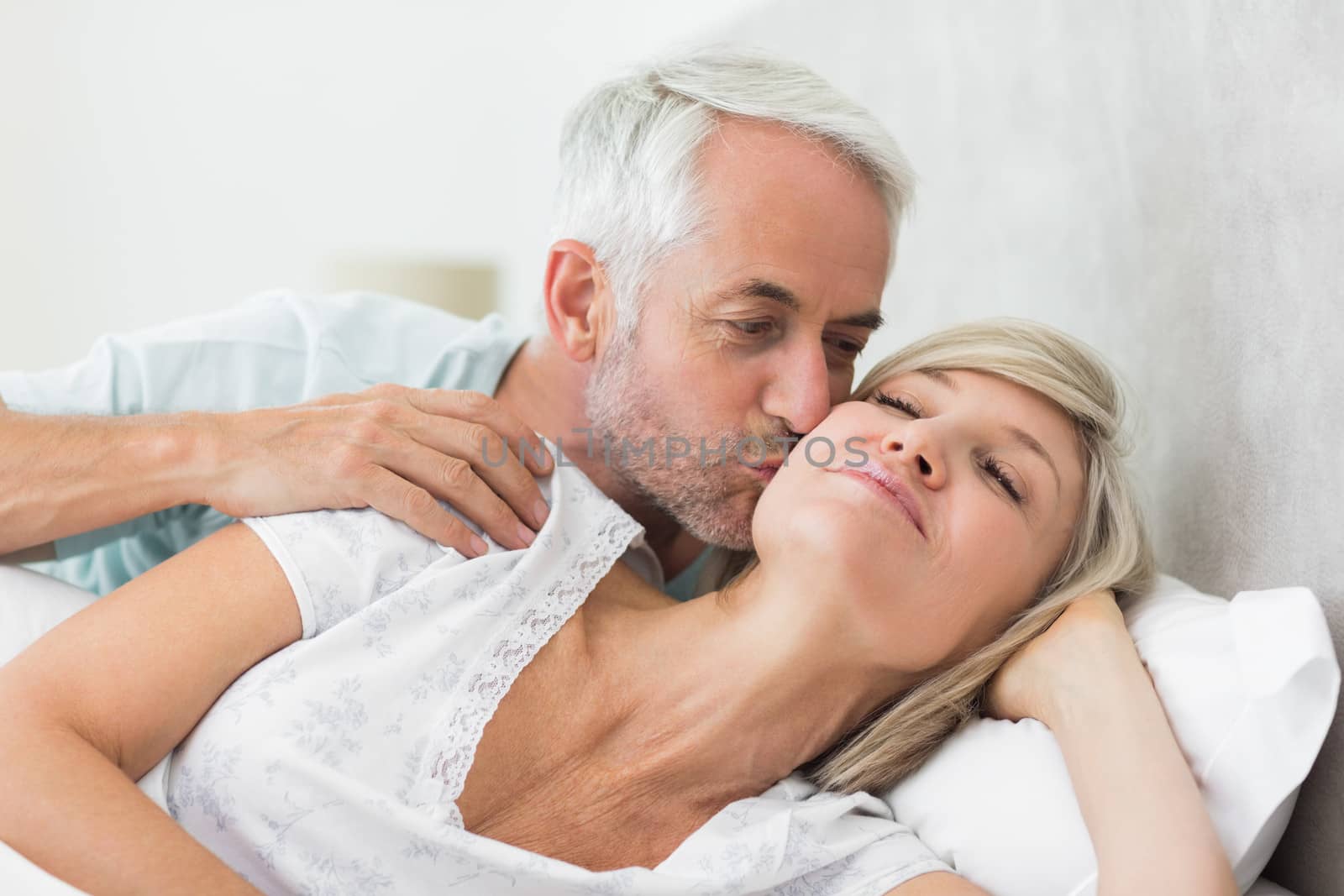 Closeup of a mature man kissing womans cheek in bed at the home