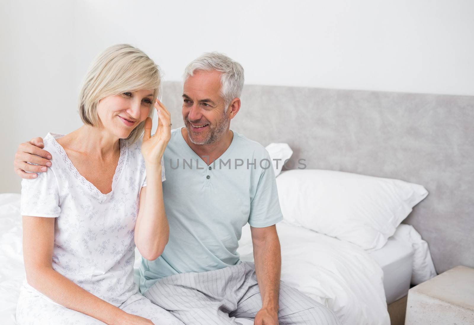 Smiling mature man and woman sitting on bed at home