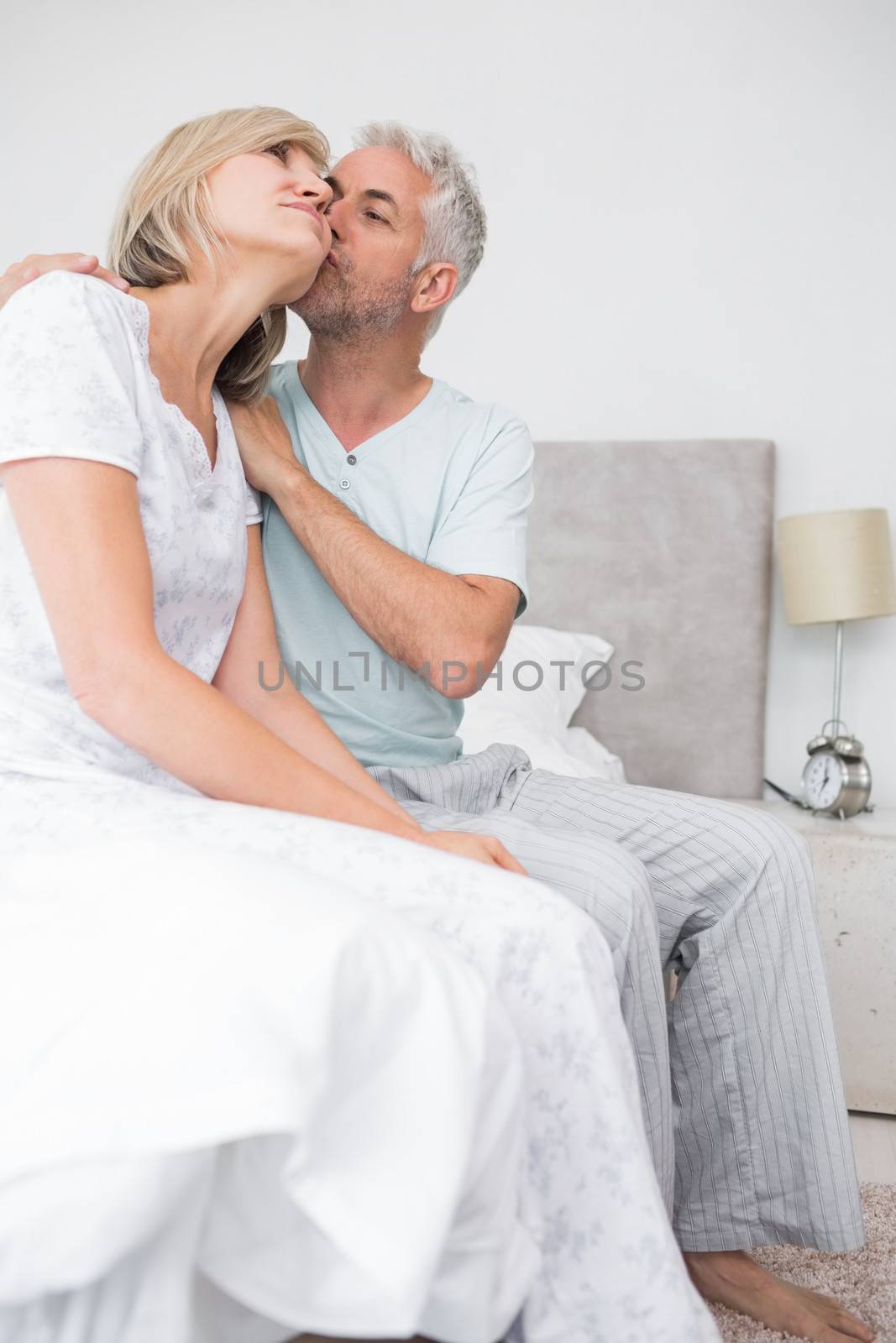 Side view of a mature man kissing womans cheek in bed at the home