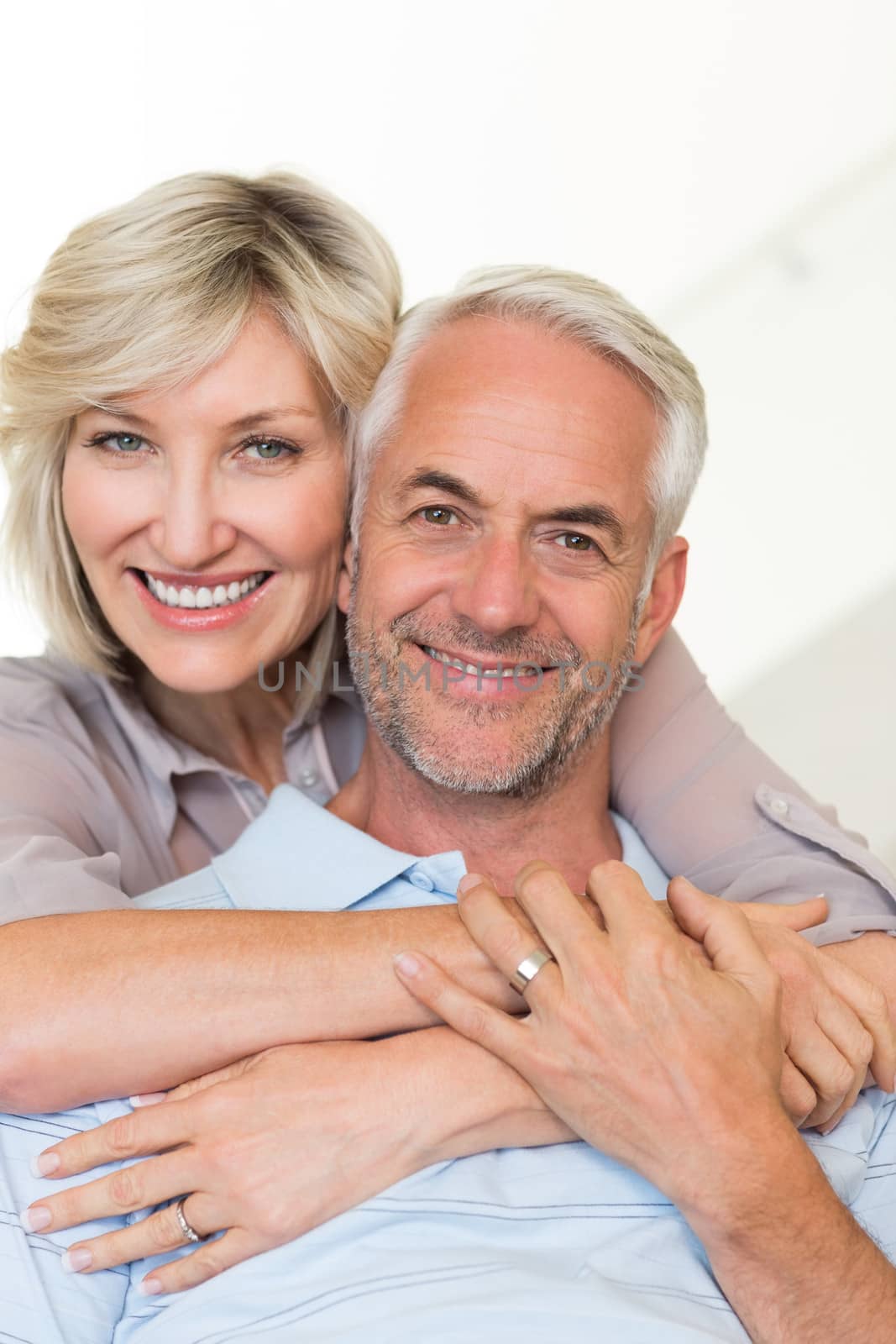 Portrait of a smiling woman embracing mature man from behind on sofa at home
