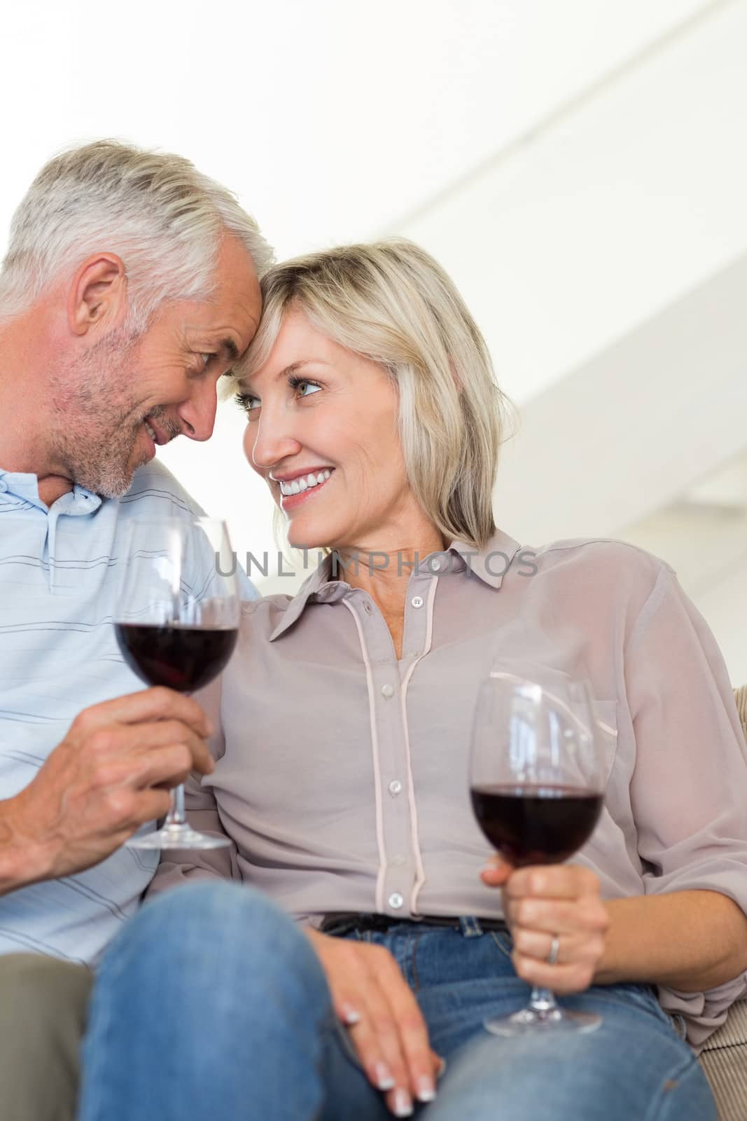 Smiling mature couple with wine glasses sitting on sofa by Wavebreakmedia