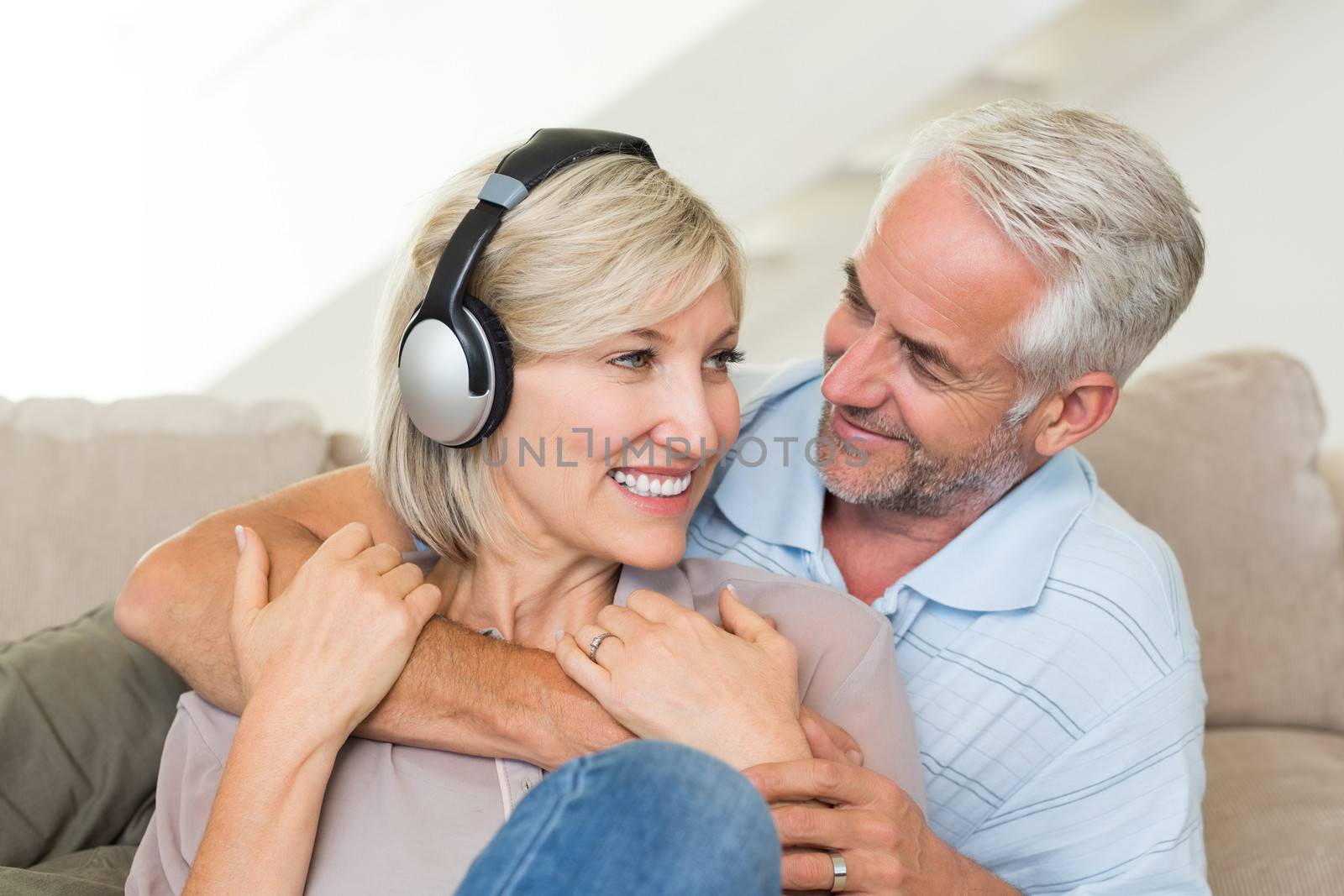Smiling mature man embracing woman from behind on sofa at home