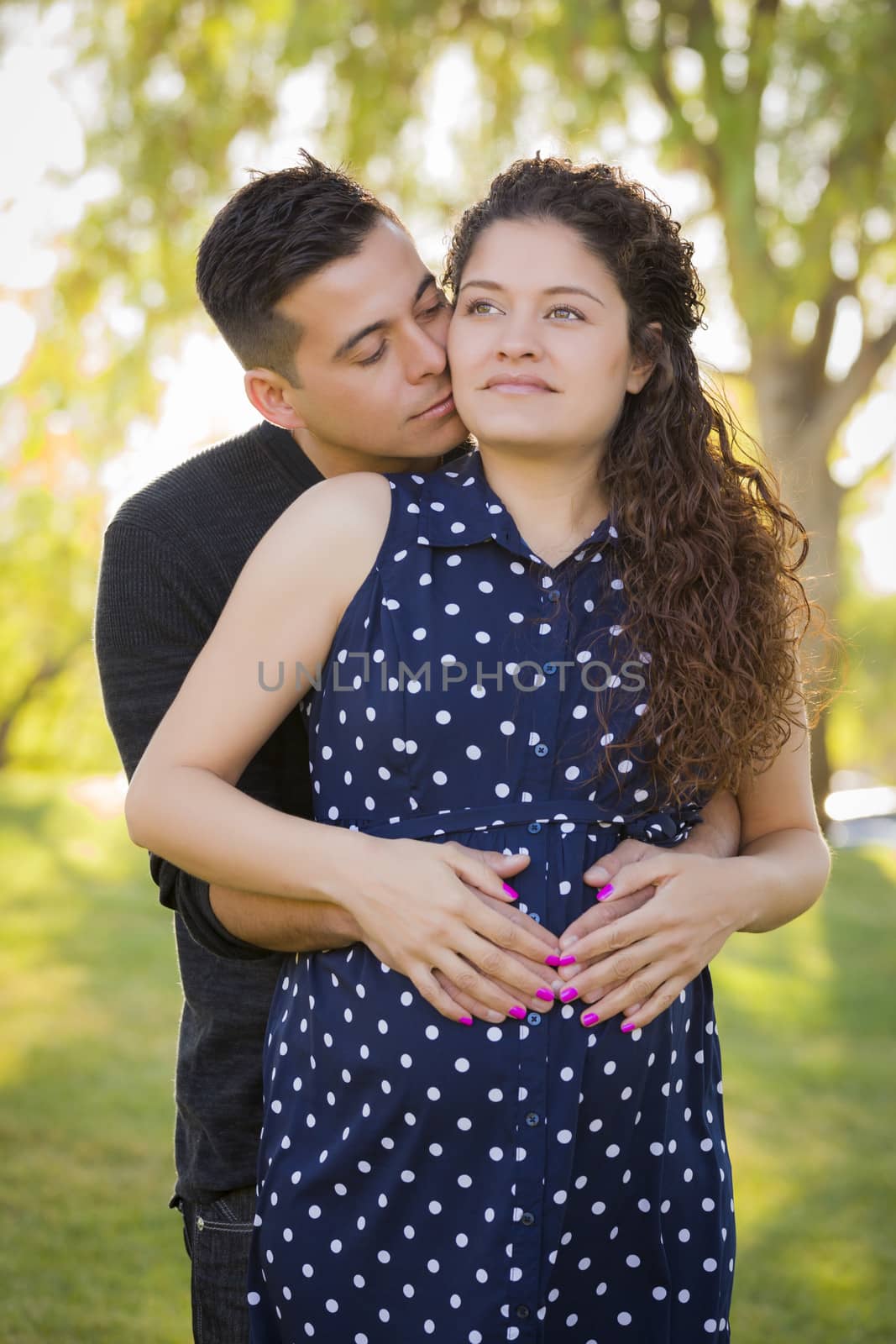 Happy Hispanic Man Hugs His Pregnant Wife Outdoors At The Park.