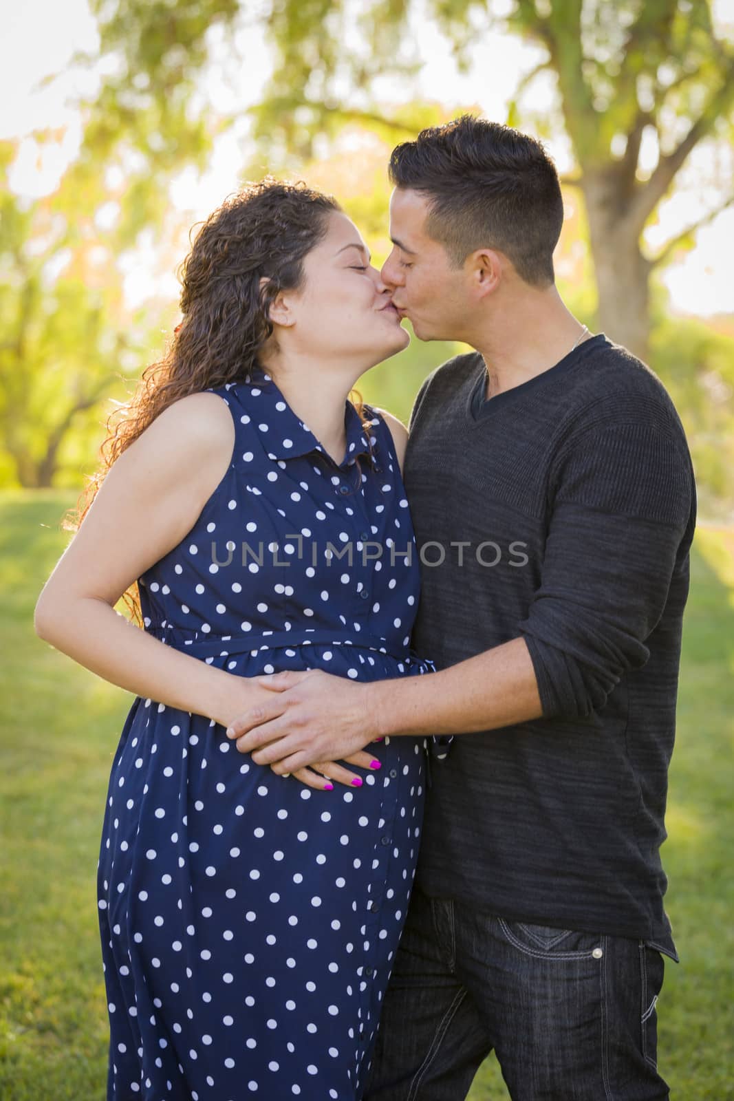 Hispanic Man Kisses His Pregnant Wife and Feels Their Baby Kick Outdoors At the Park.