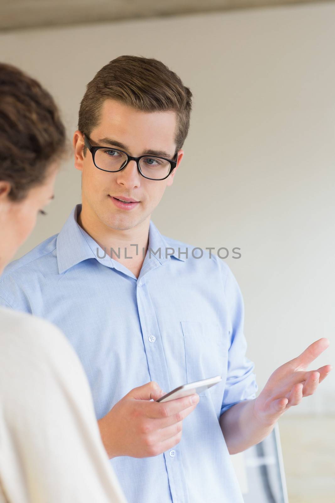 Young businessman holding mobile phone while communicating with female colleague in office