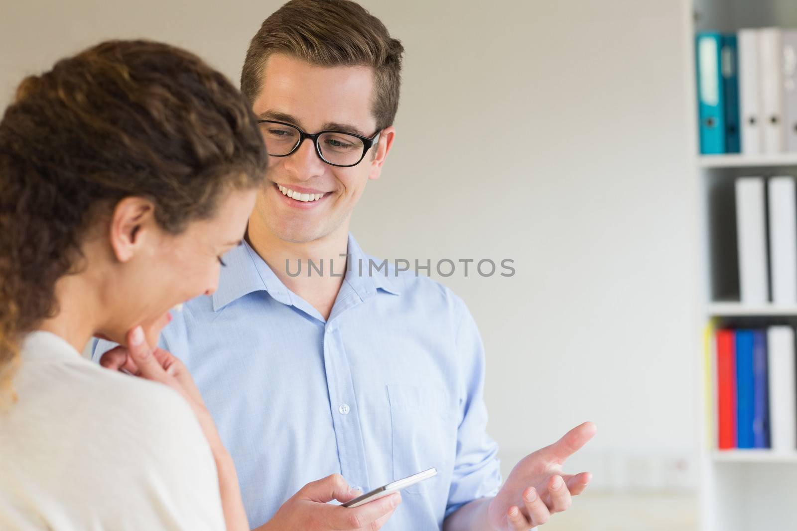 Young businessman holding mobile phone while looking at female colleague in office