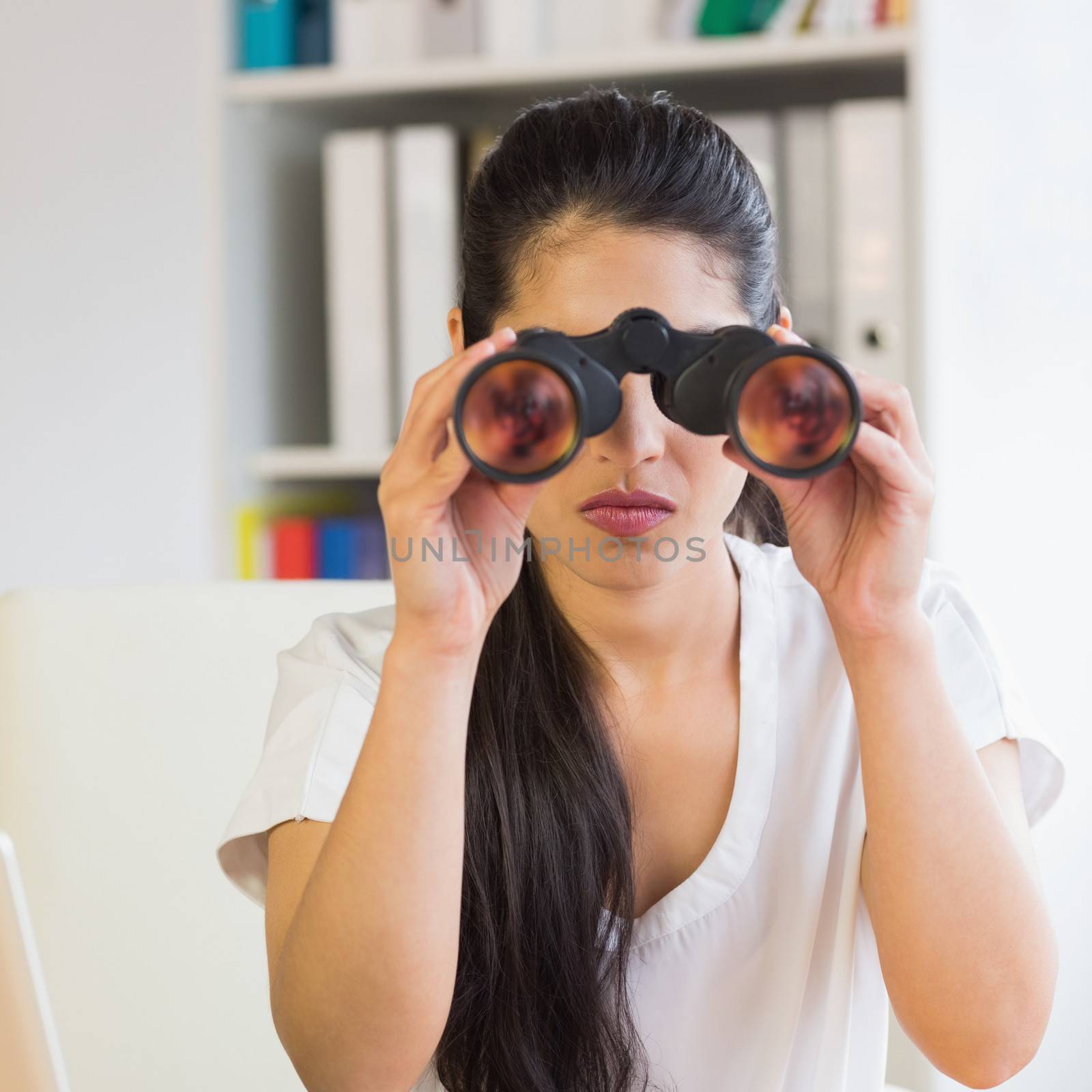 Young determined businesswoman looking through binoculars in office