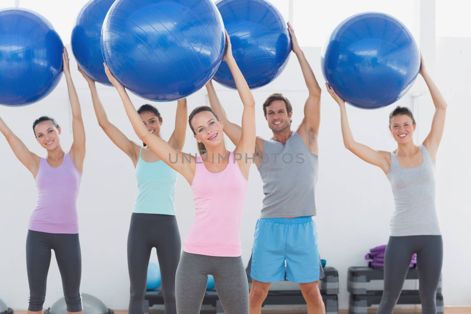 Fitness class holding up exercise balls at fitness studio by Wavebreakmedia