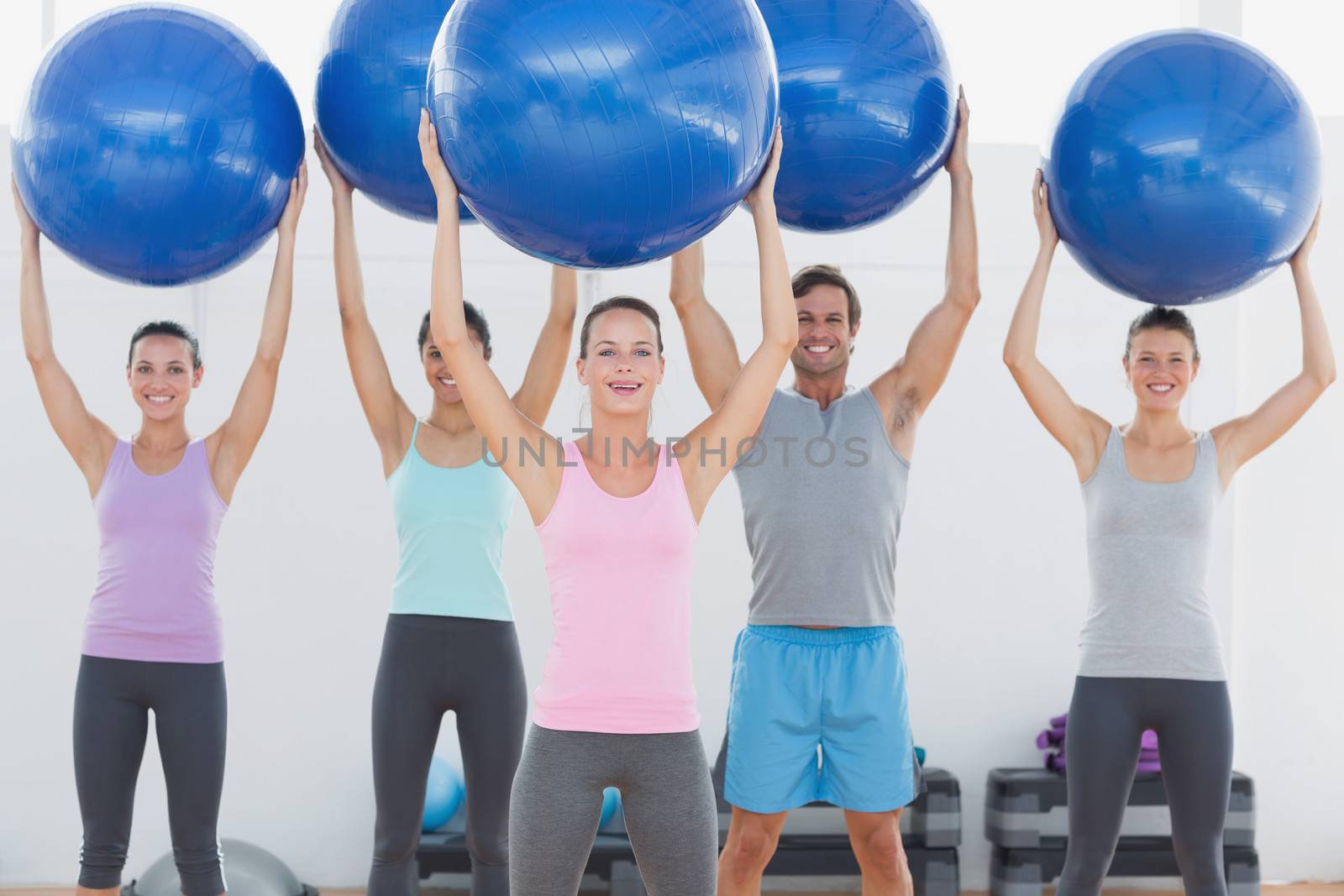 Portrait of an instructor and fitness class holding up exercise balls at the fitness studio