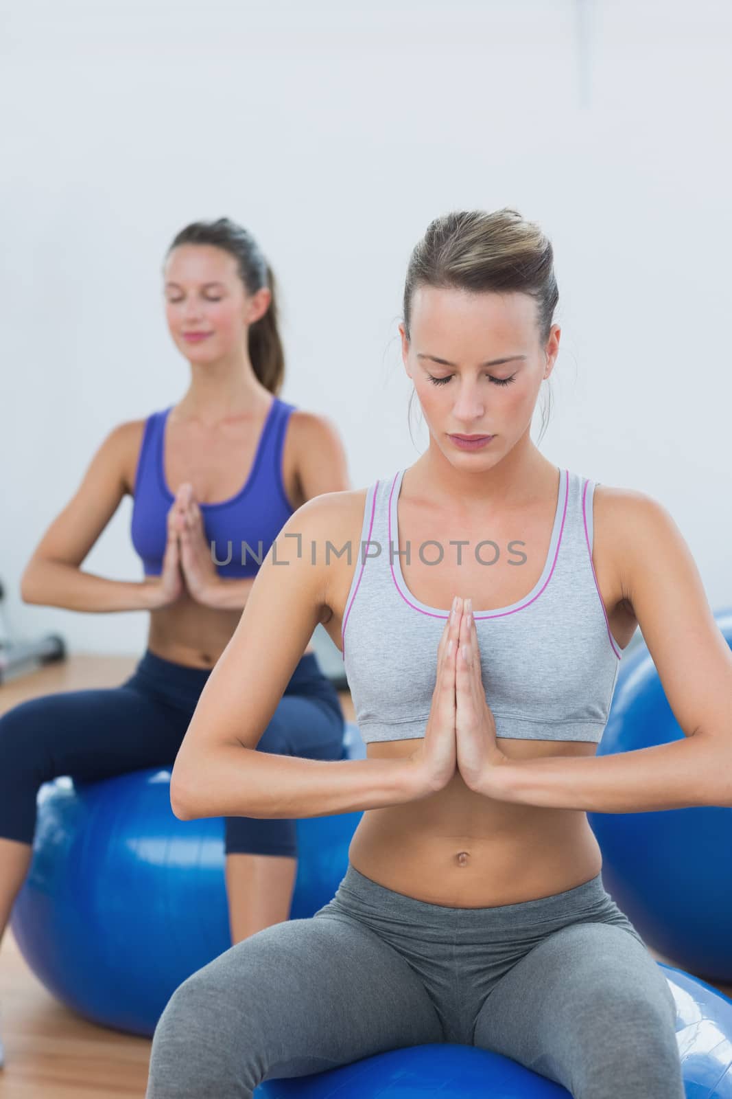 Women with joined hands and eyes closed on exercise balls by Wavebreakmedia