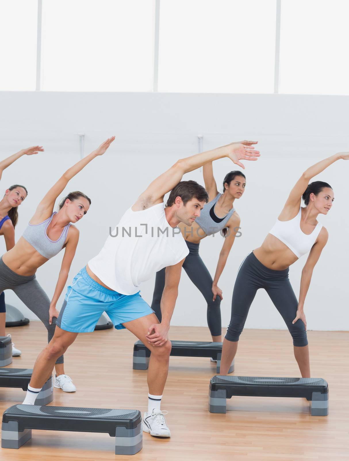 Class doing stretching exercise in fitness studio by Wavebreakmedia