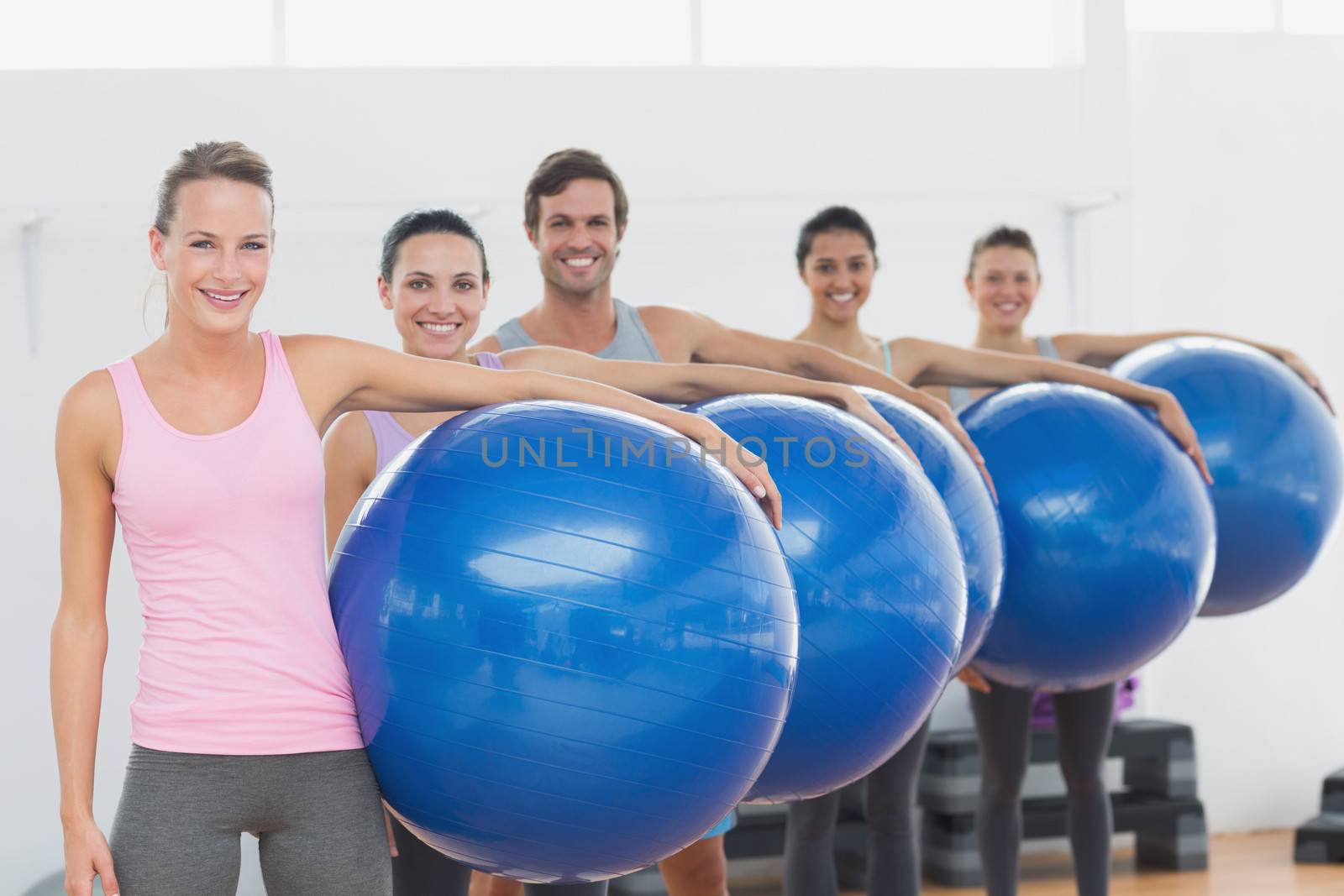 Portrait of an instructor and fitness class holding exercise balls at fitness studio