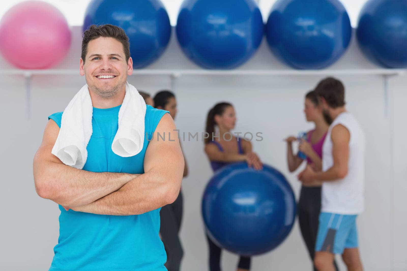 Portrait of a fit smiling young man with friends in background at fitness studio
