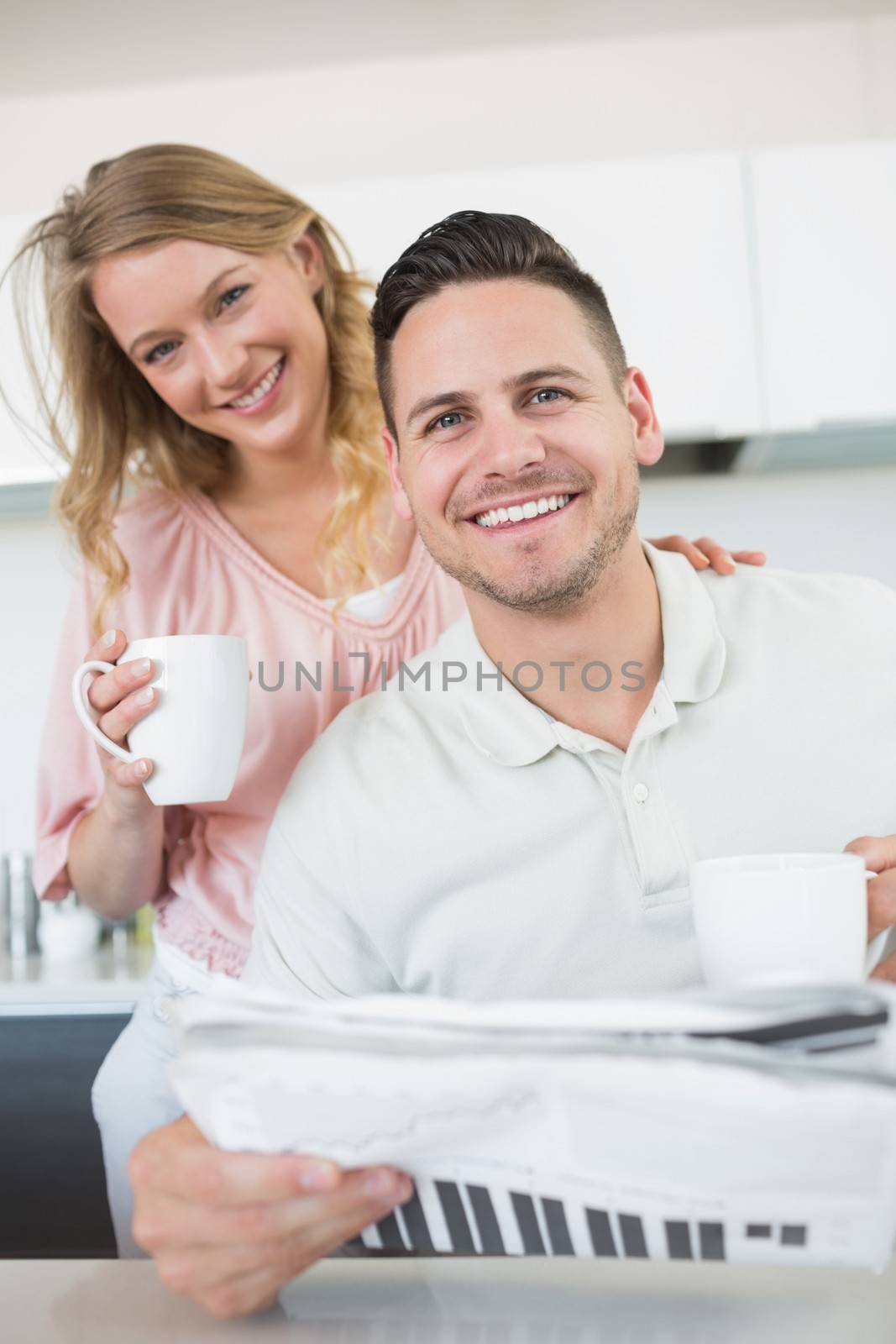 Couple with coffee mugs and newspaper in kitchen by Wavebreakmedia