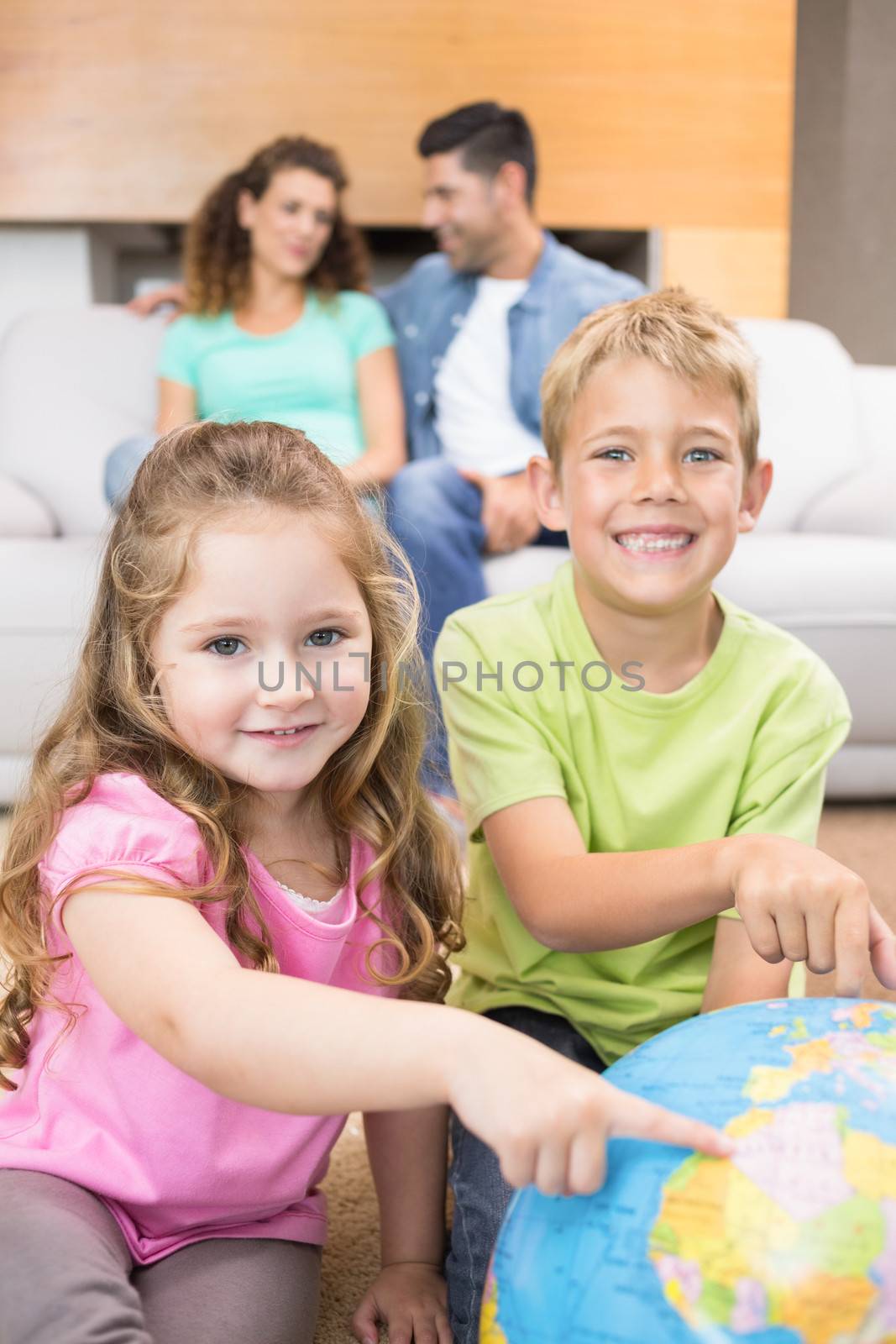 Smiling siblings pointing to globe on the rug at home in living room