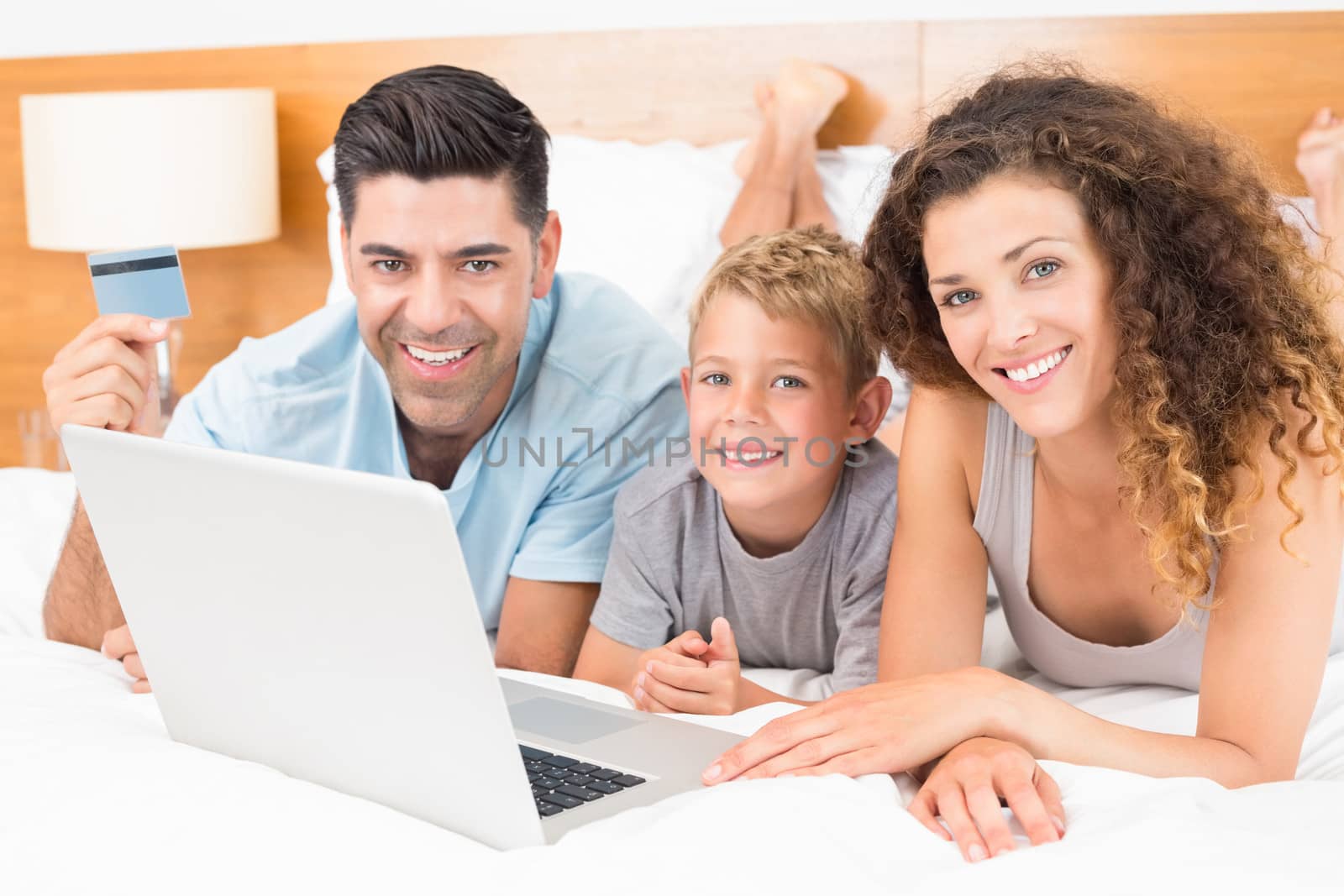 Smiling young family using laptop to shop online together on bed at home in bedroom