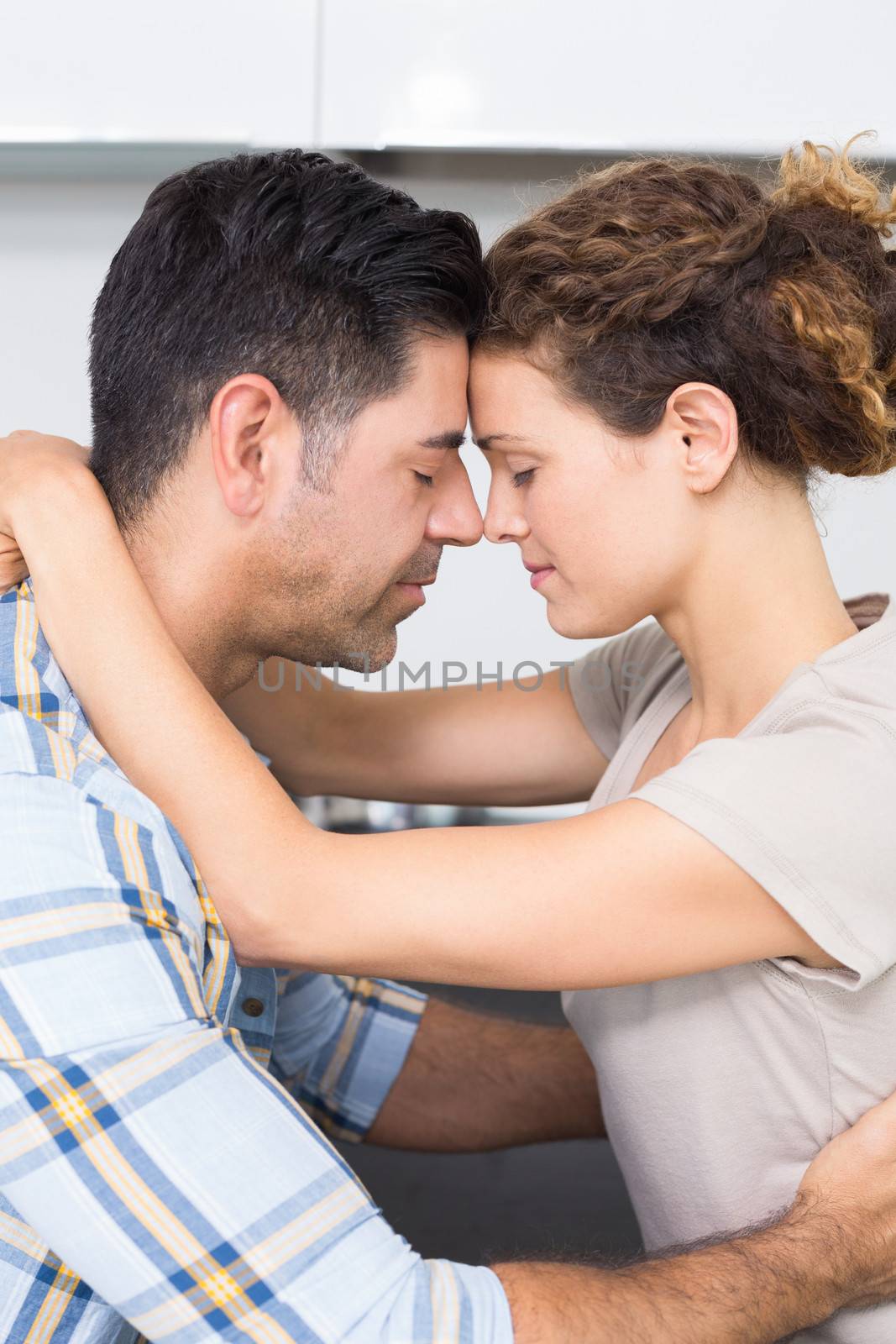 Romantic couple hugging with eyes closed at home in kitchen