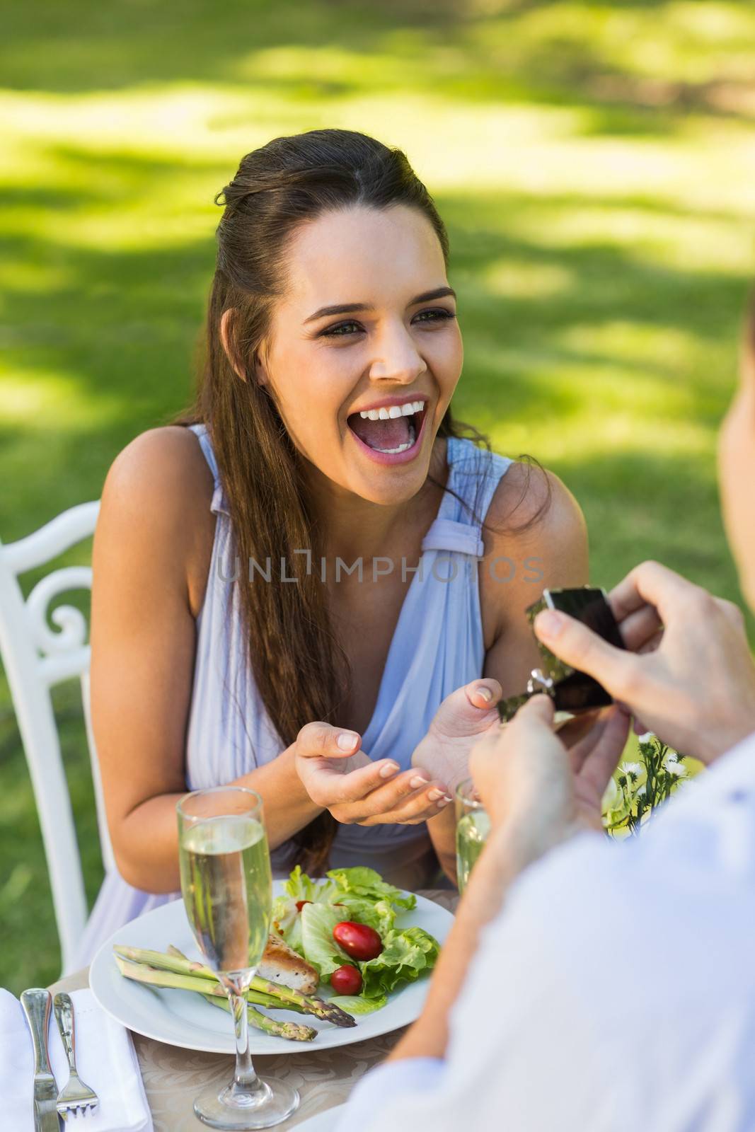 Man proposing a cheerful woman while they have a romantic date at an outdoor caf├®