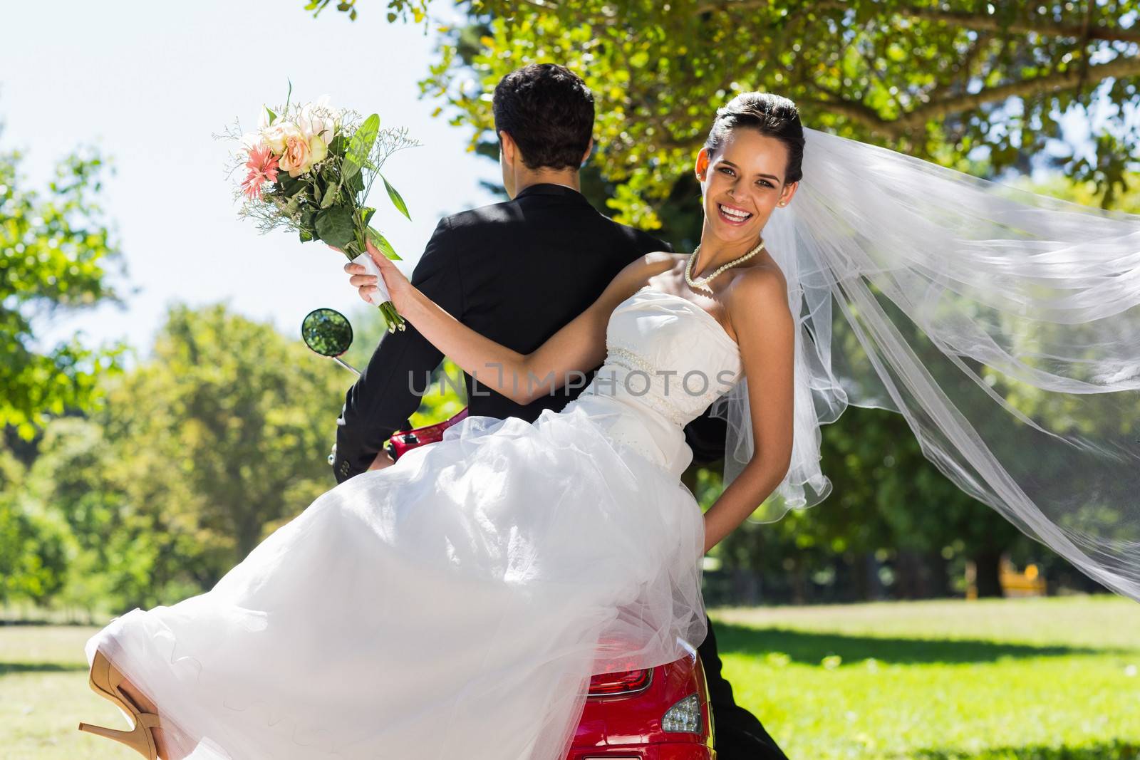 Newlywed couple sitting on scooter in park by Wavebreakmedia