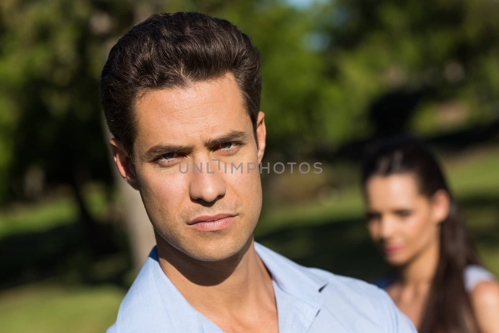 Close-up of a young man with blurred woman in the background outdoors