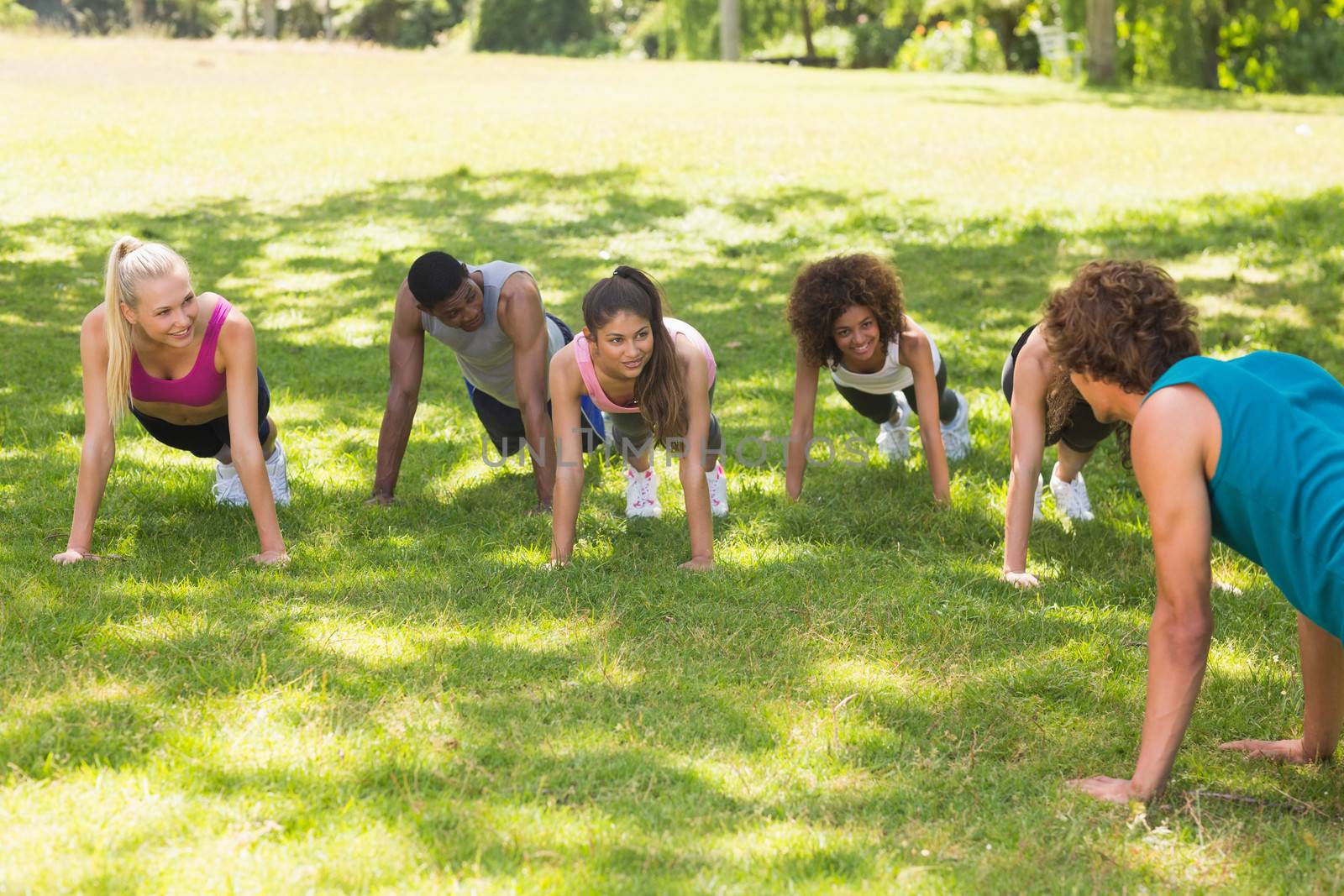 Instructor with group of fitness class doing push ups in the park