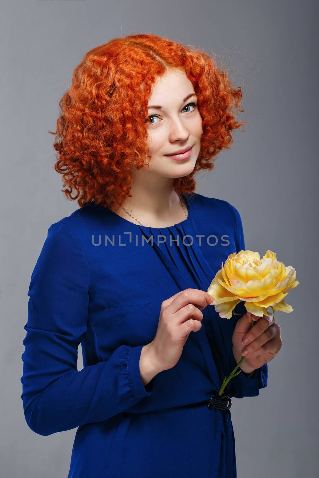 Attractive young red-haired girl in a blue dress holding in her hands a yellow flower
