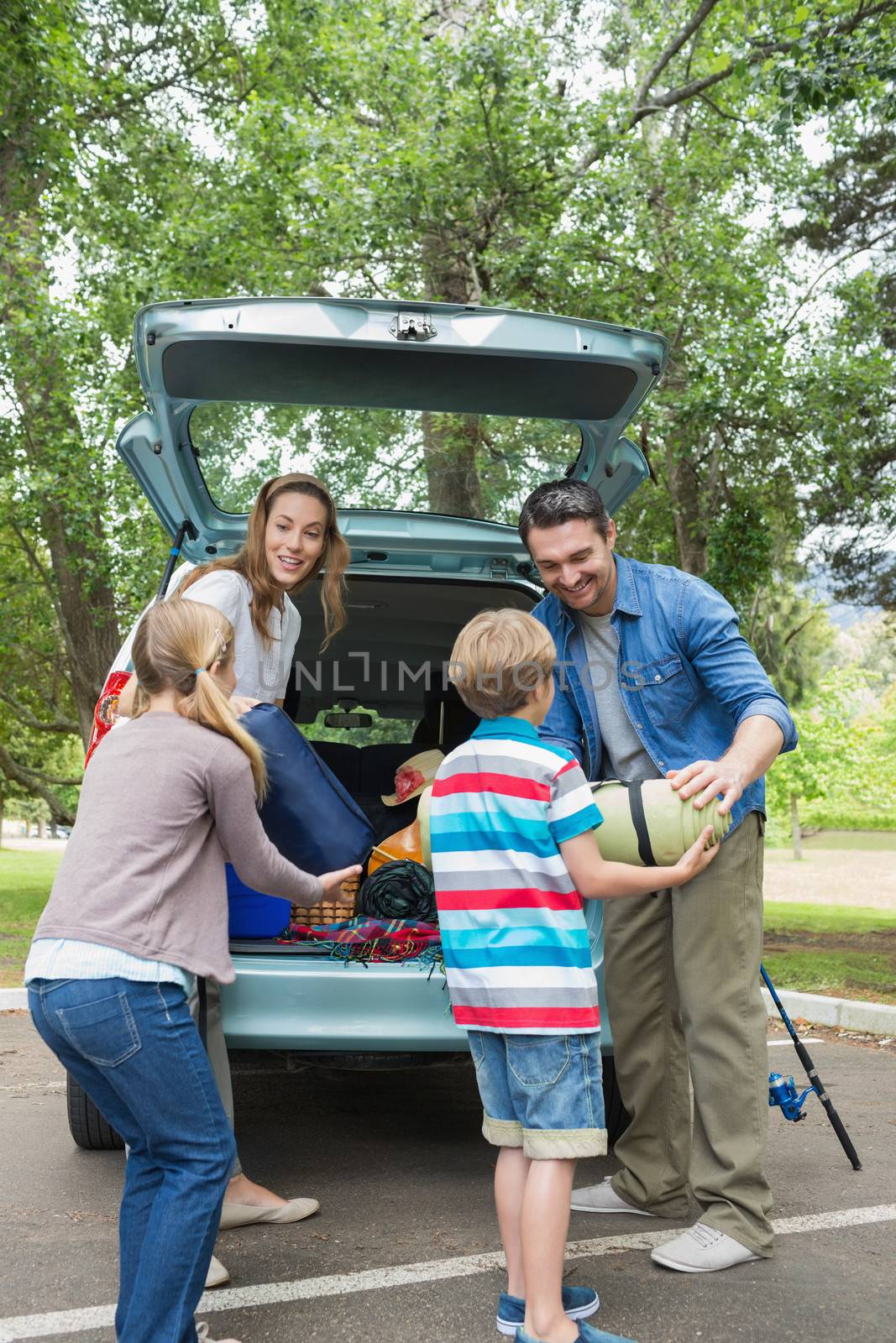 Happy family of four unloading car trunk while on picnic