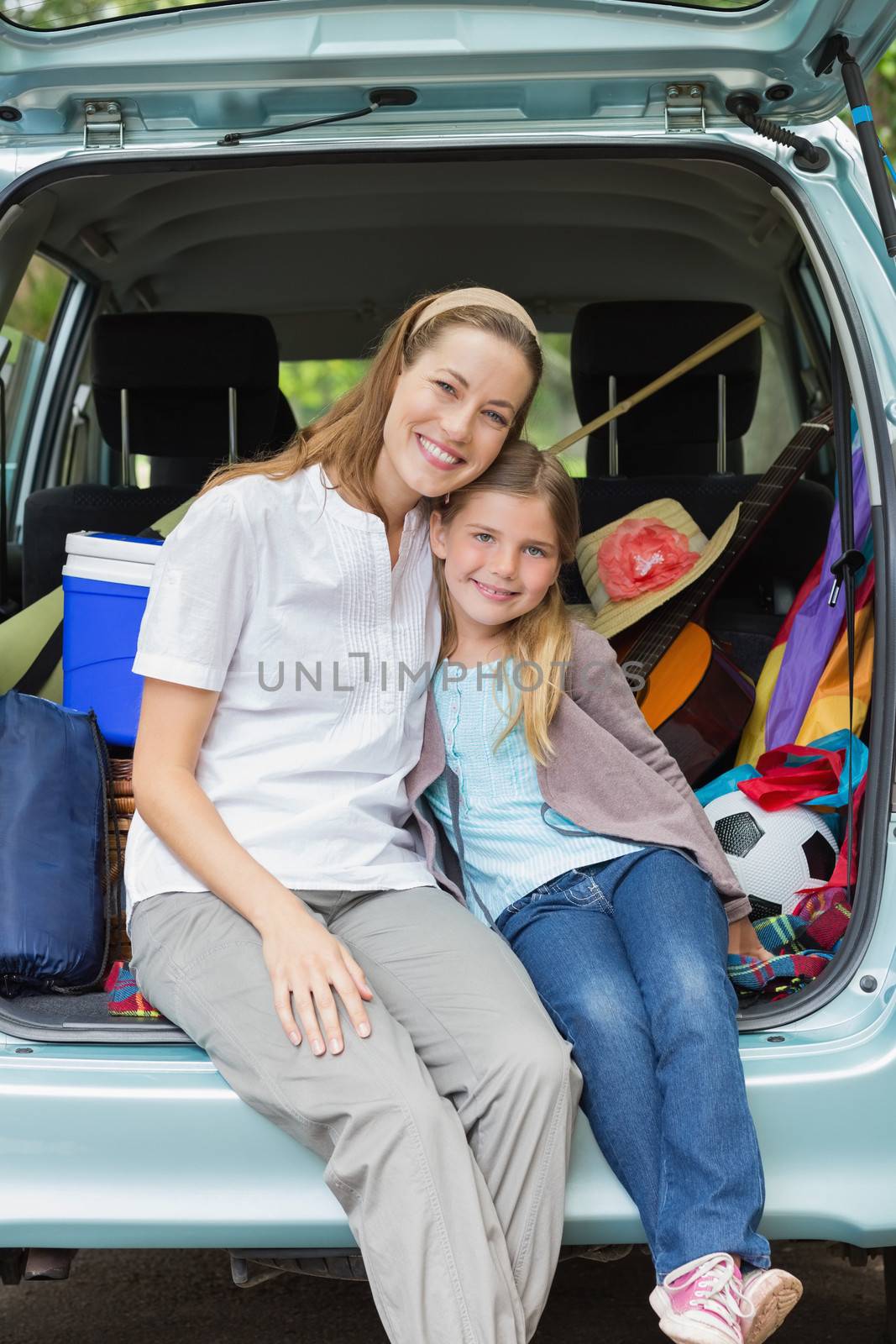 Smiling mother and daughter sitting in car trunk by Wavebreakmedia