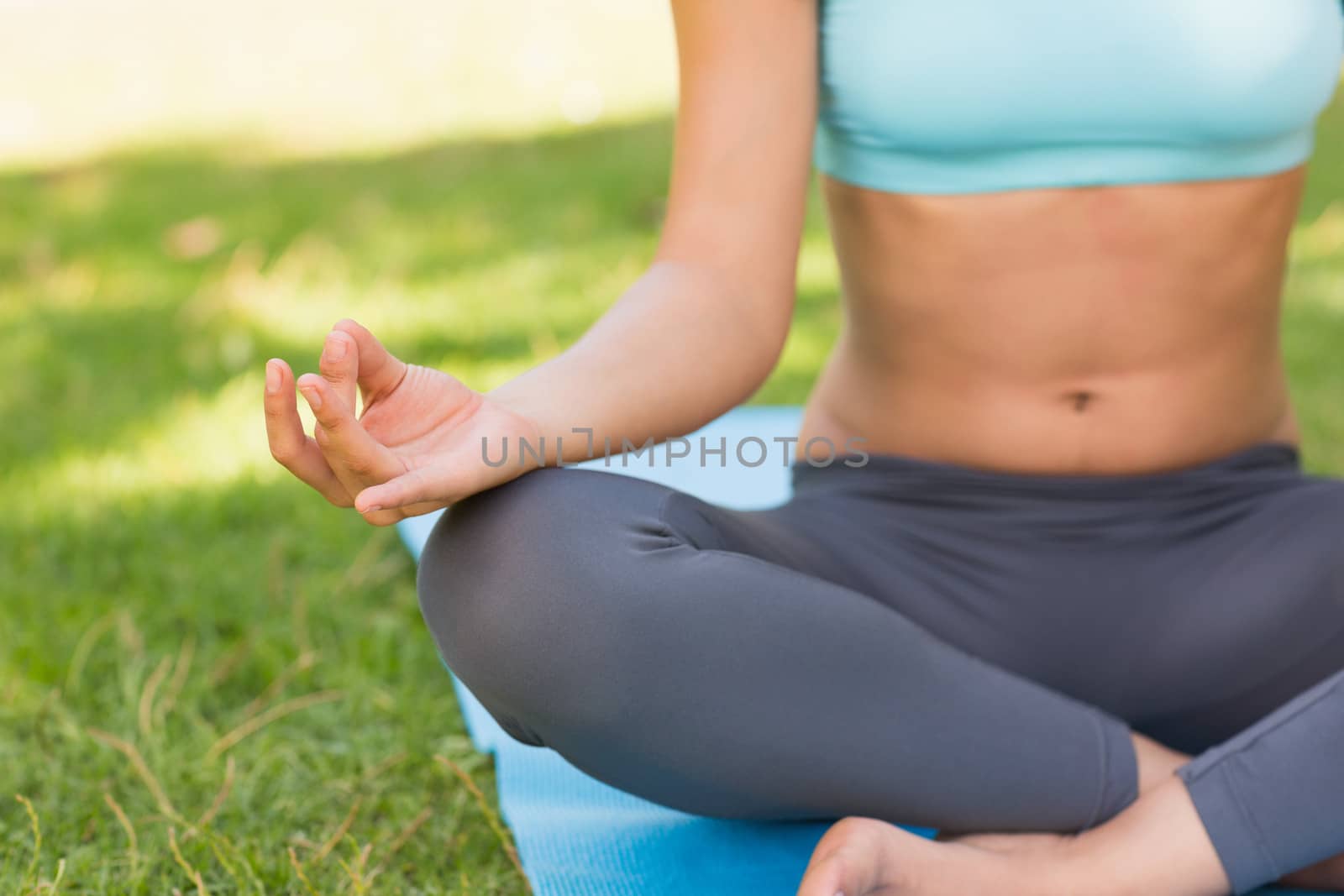 Close-up mid section of a sporty young woman in lotus pose at the park