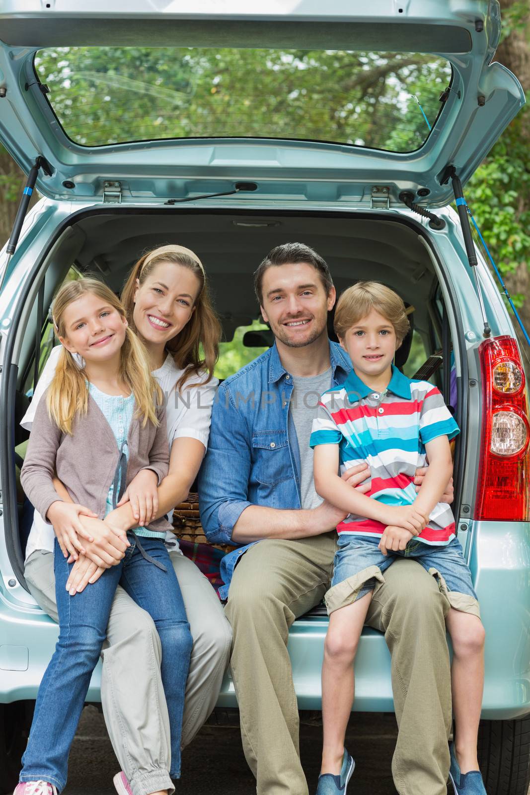 Happy family of four sitting in car trunk by Wavebreakmedia