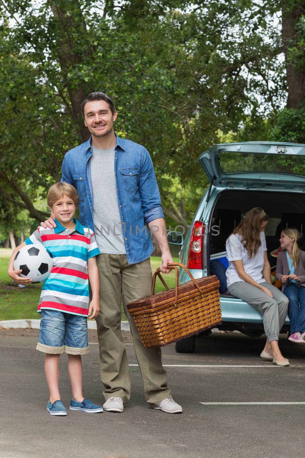 Portrait of father and son with picnic basket while mother and daughter sitting in car trunk