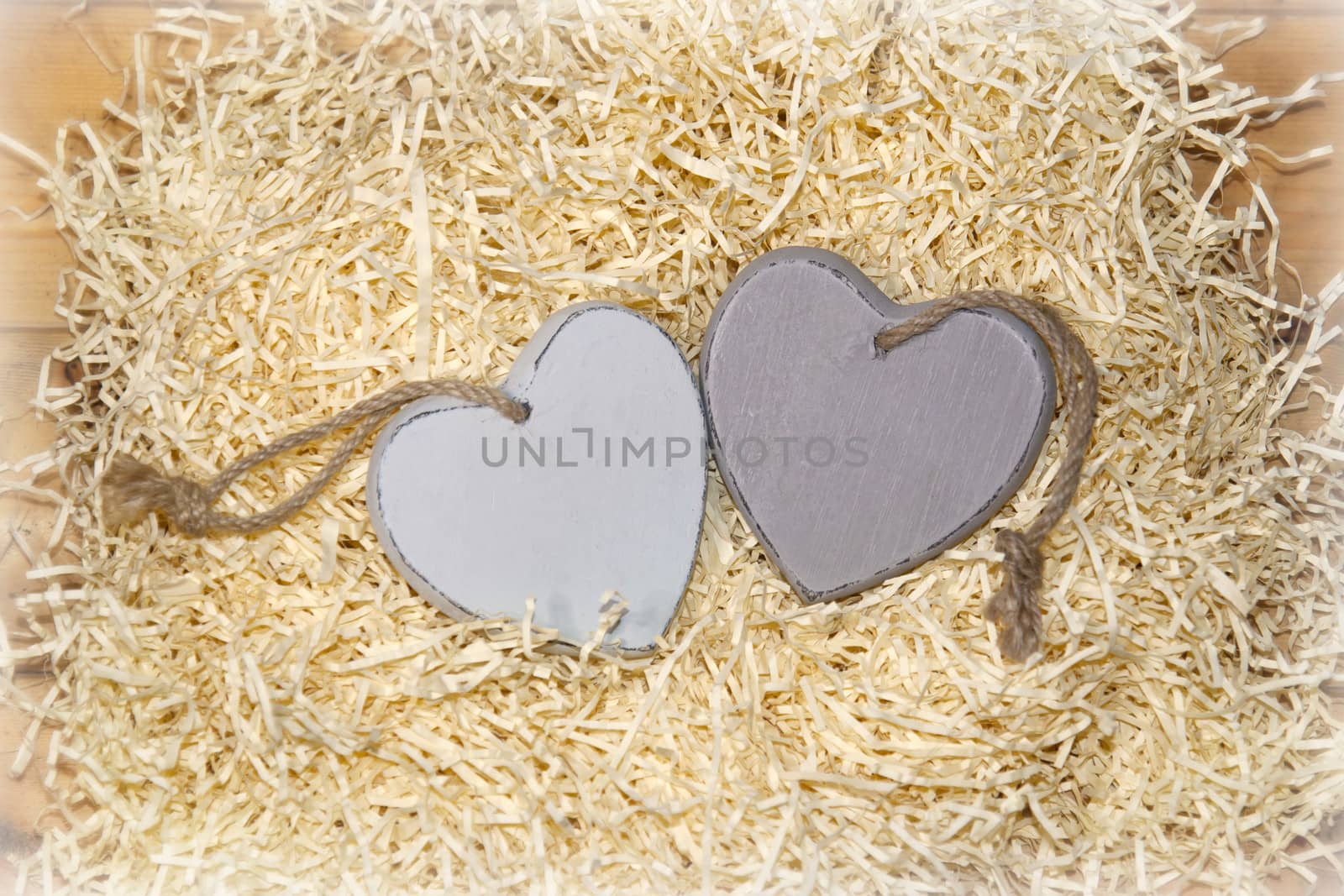 two wooden hearts in a love nest made of straw on a wooden background