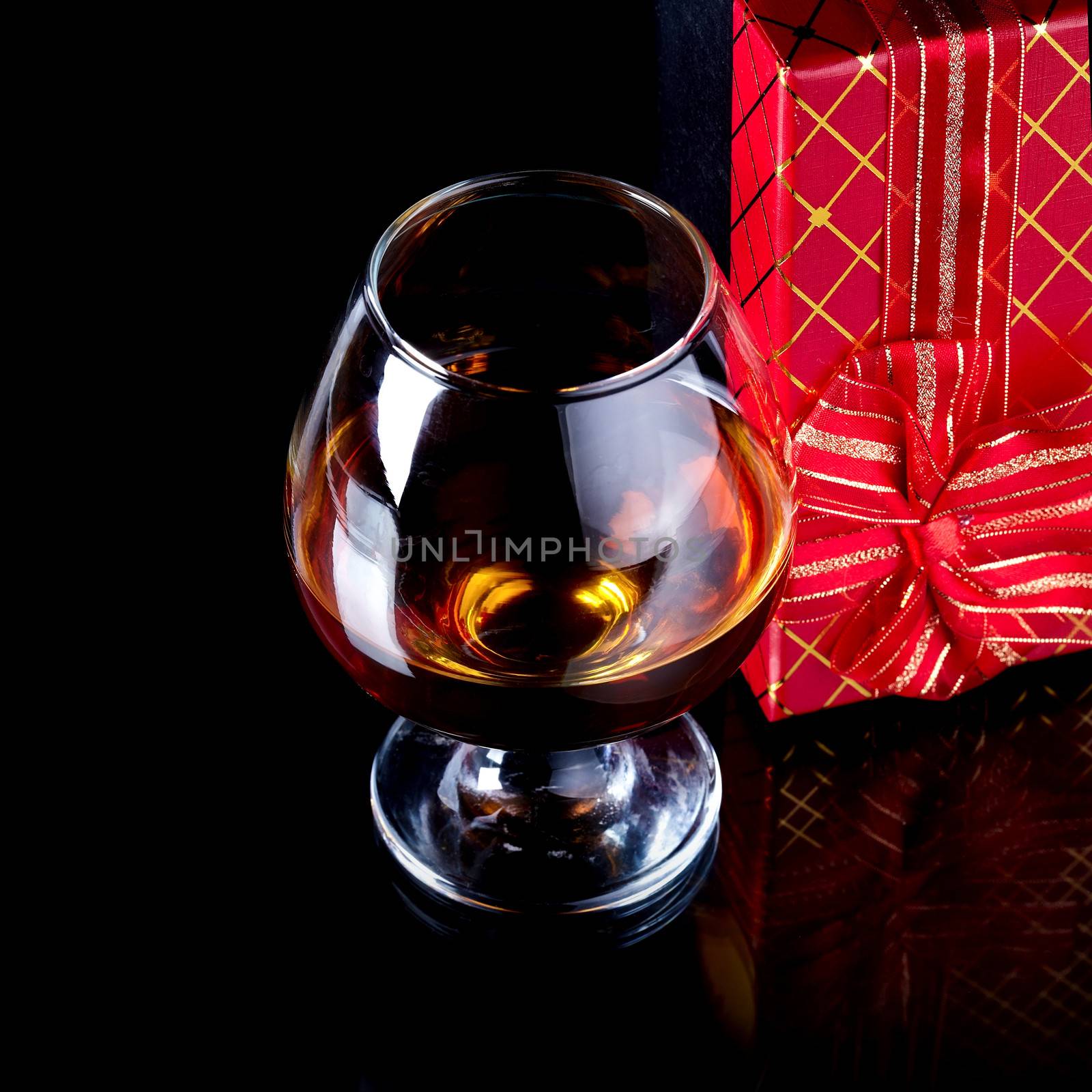 Glass with alcohol and a gift. Alcohol and gift box. Box with a bow and glass with drink.