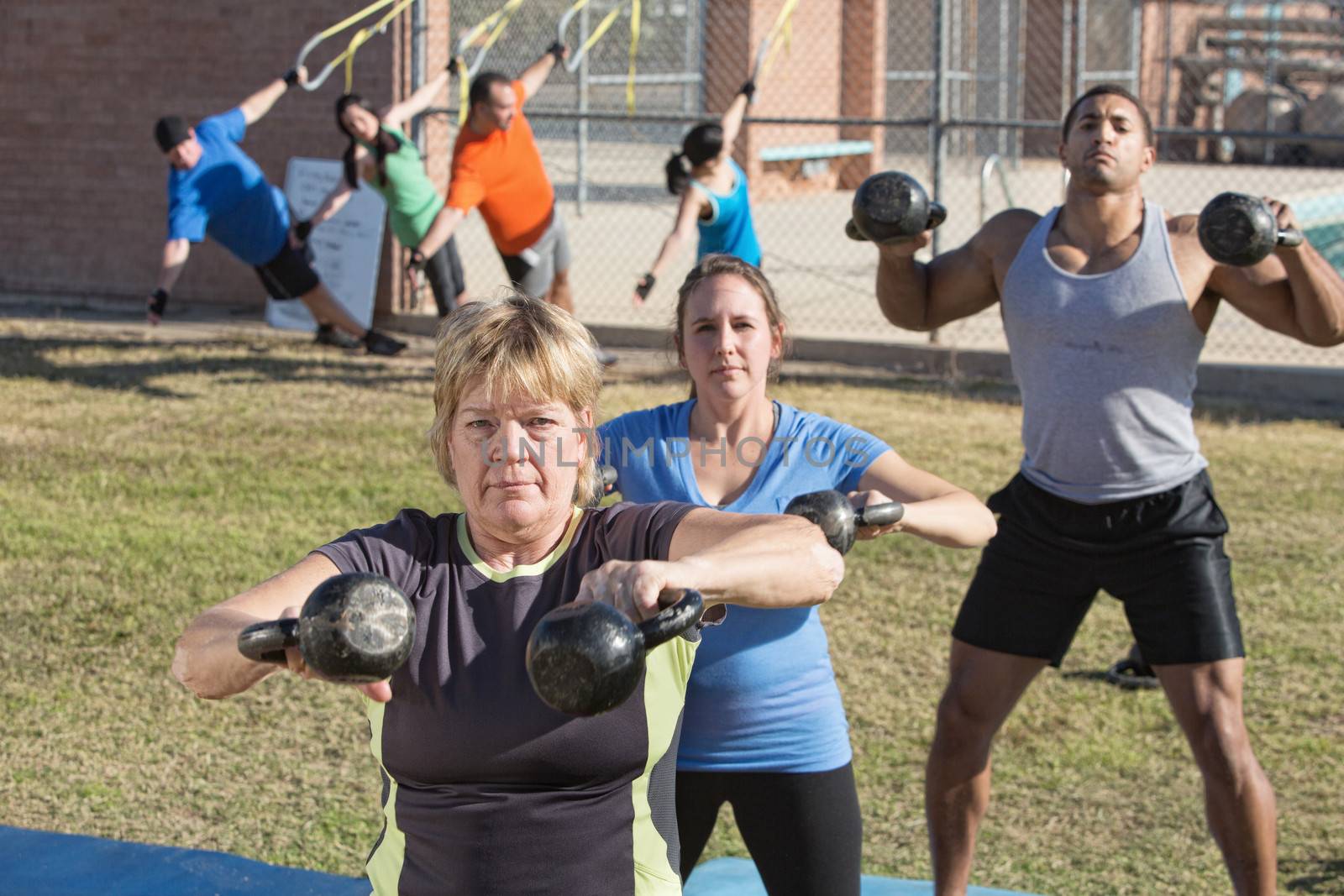 Mature woman and group exercising in outdoor boot camp fitness class