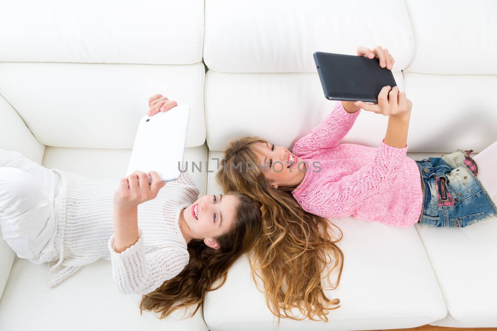 kid girls having fun playing with tablet pc lying sofa by lunamarina