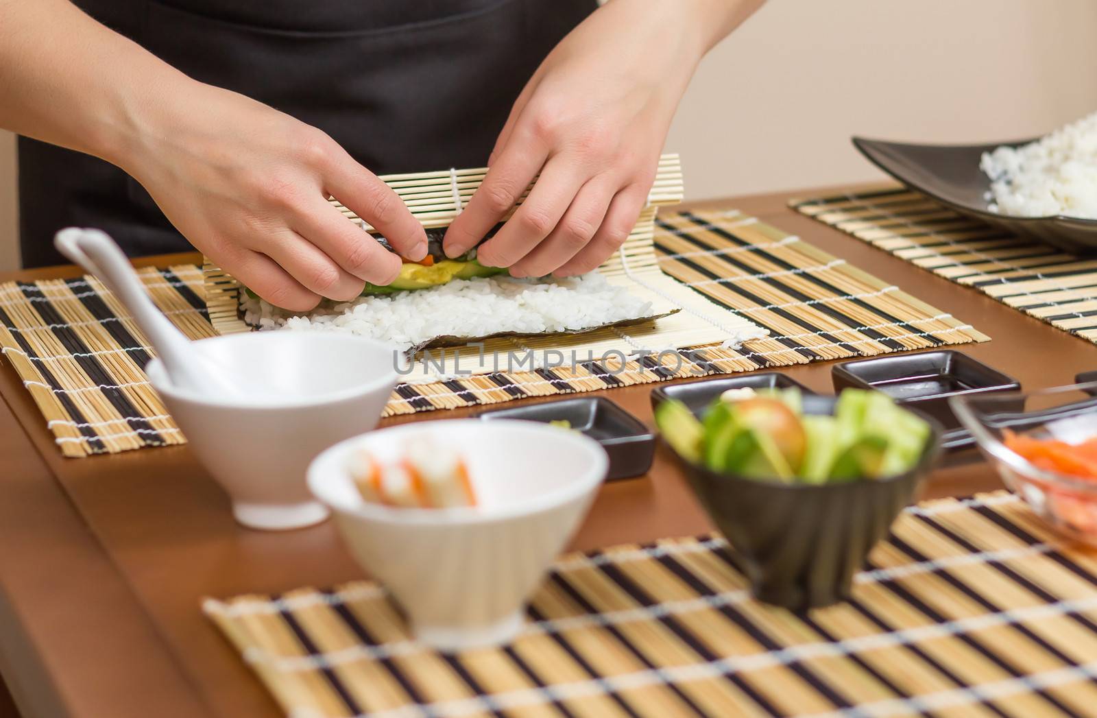 Hands of woman chef rolling up a japanese sushi with rice, avocado and shrimps on nori seaweed sheet