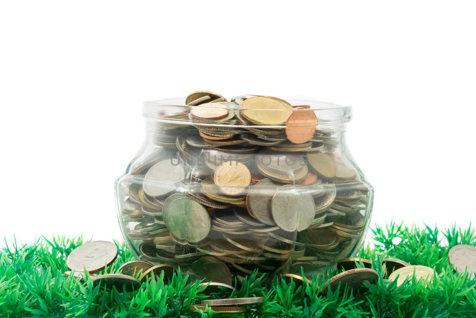 glass jar full of bath coins on artificial grass on white background