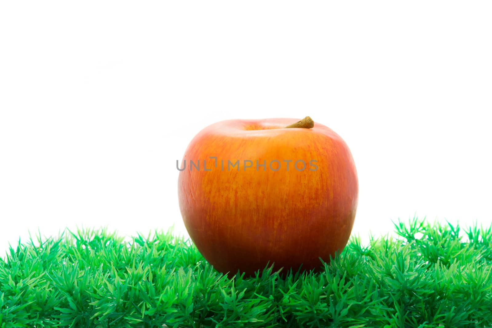 Red apple in green artificial grass on white background