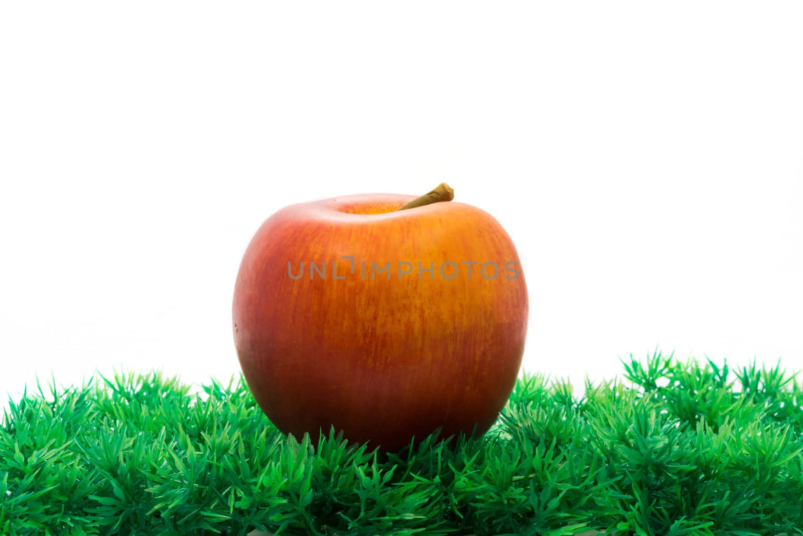 Red apple in green artificial grass on white background