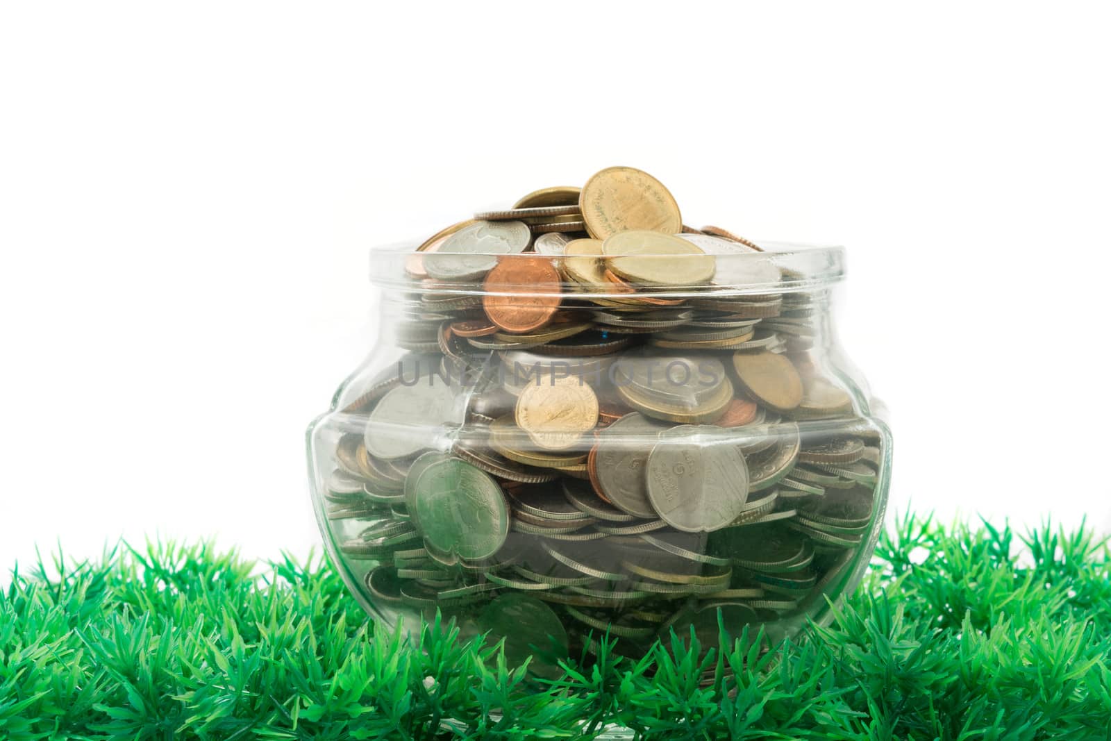 glass jar full of bath coins on artificial grass on white background